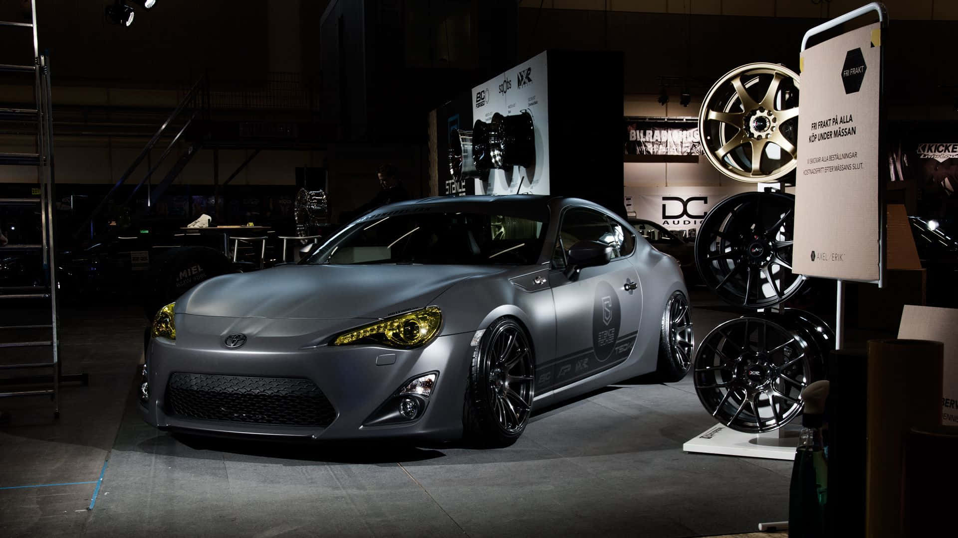 消光灰色跑車，黃色頭燈，在燈光昏暗的車展中展示。 — Toyota Supra Mk4 壁紙