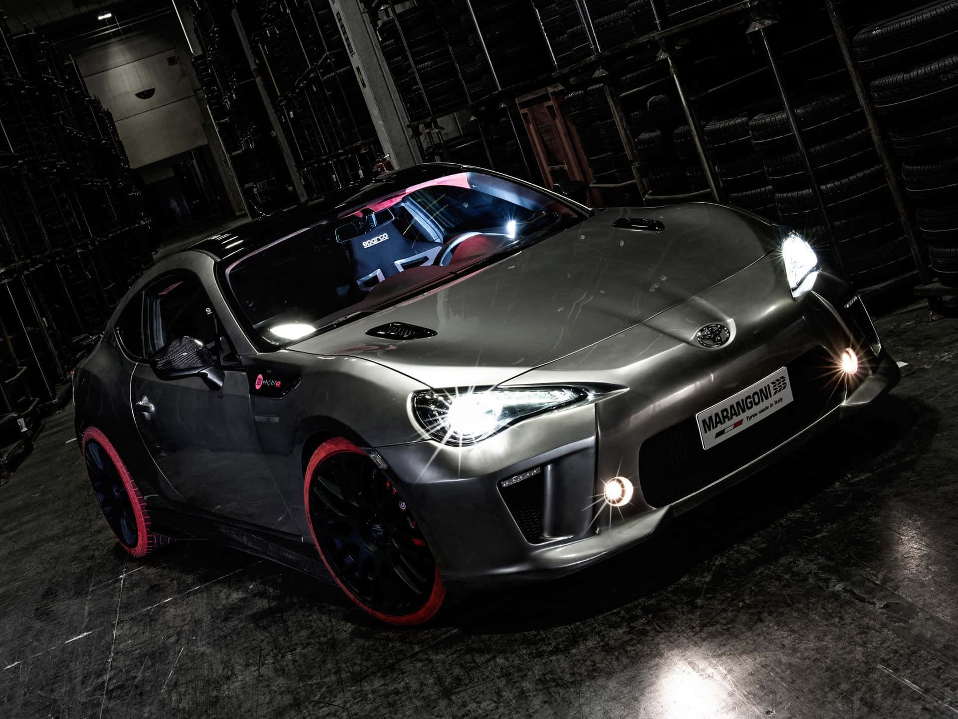 客製灰色跑車，紅色輪圈，停在一個充滿輪胎的車庫裡。 — Toyota Supra Mk4 壁紙