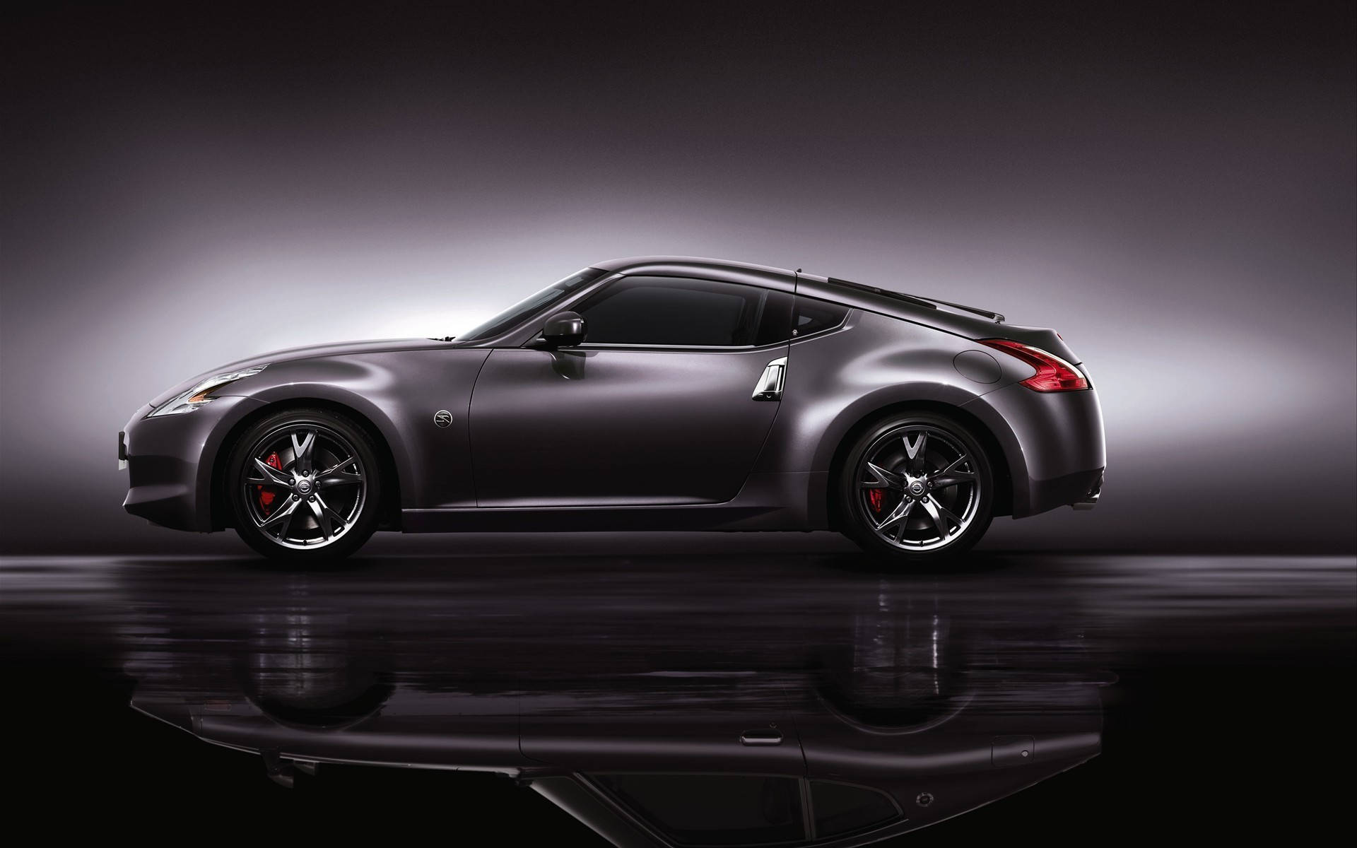 Nissan 桌布 壁紙 — 一輛時尚的消光灰色跑車配備紅色制動卡鉗，在帶有戲劇性燈光和反射地板的攝影棚中展示。