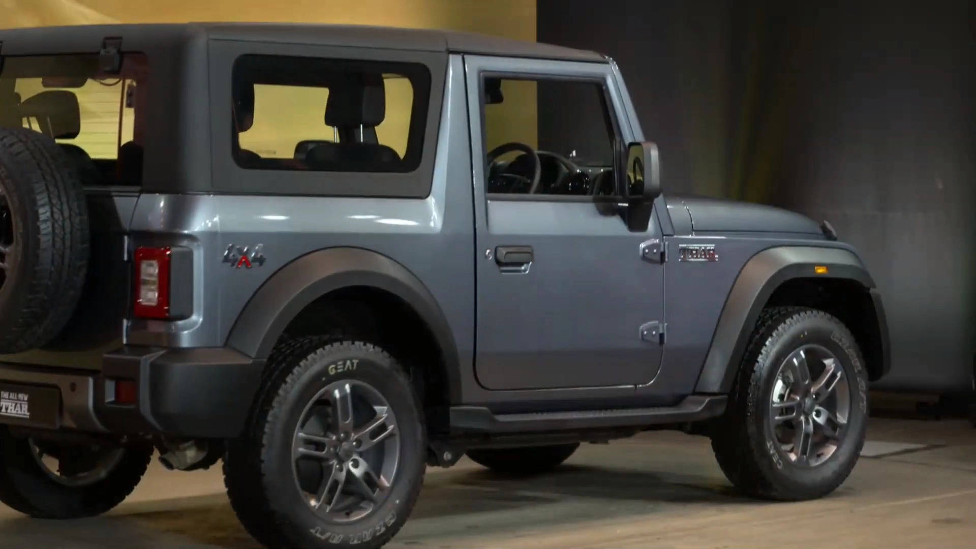 高清 桌布 壁紙 — 一輛時尚的消光灰色鈴木 Jimny SUV，帶有黑色飾邊和安裝在後門上的備用輪胎，停在光線昏暗的車庫中。