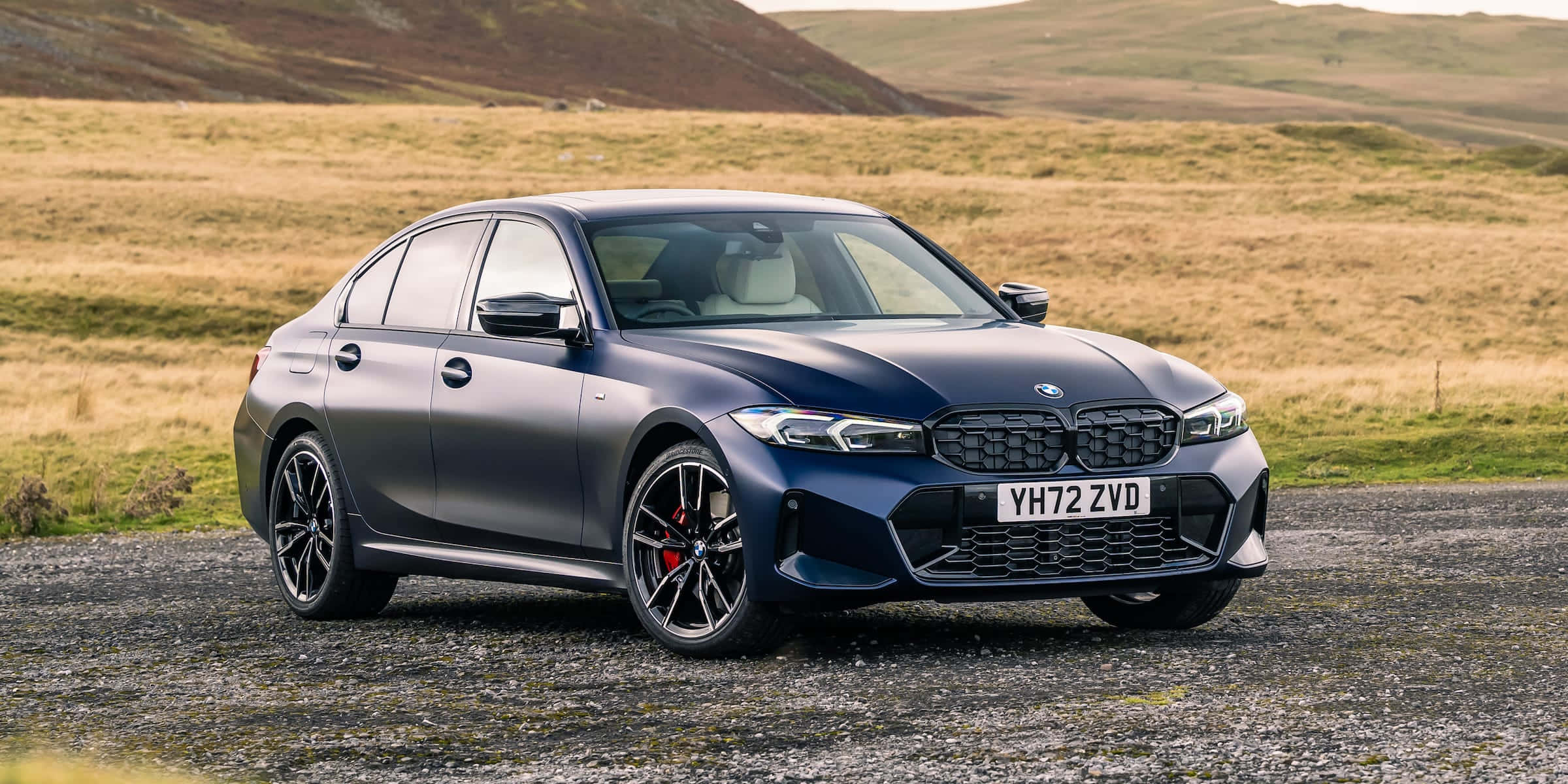Bmw 3 Series 桌布 壁紙 — 一輛時尚的消光藍色BMW 3系列轎車停在碎石路上，背景是起伏的金色山丘。