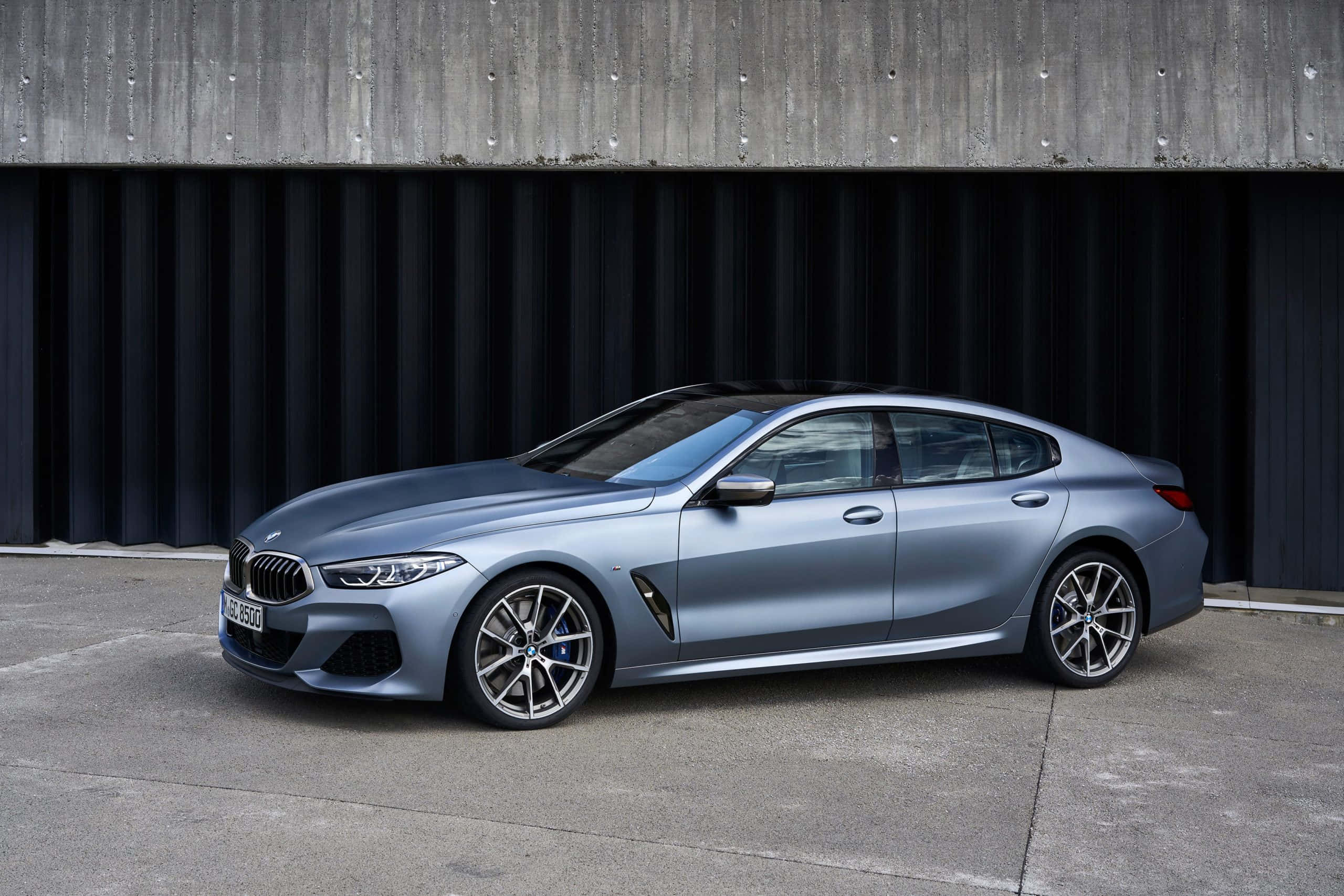 Bmw 8 Series 桌布 壁紙 — 一輛時尚的消光藍色BMW 8系列轎跑車停放在現代混凝土和深色金屬牆前。