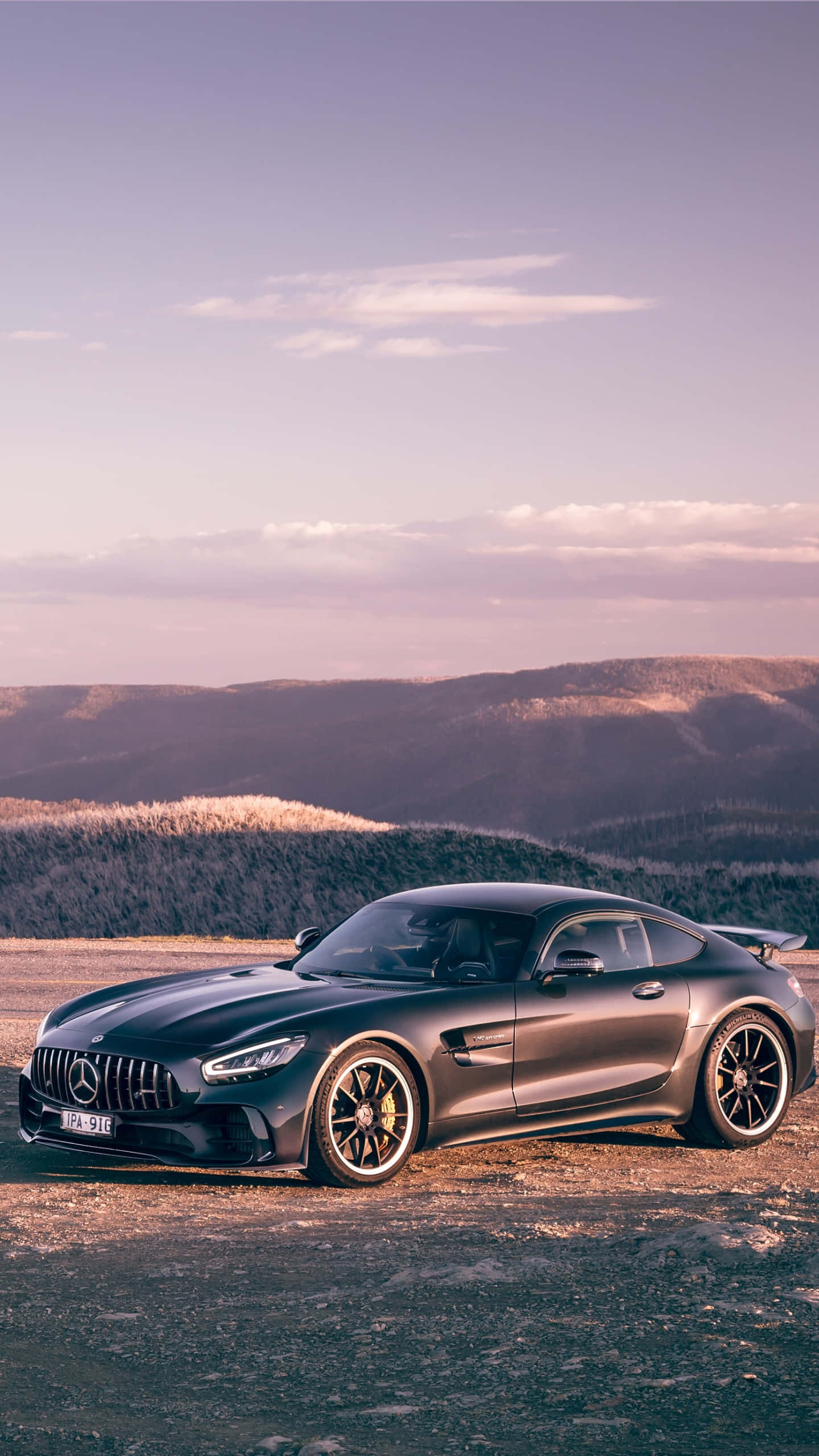 黑色 桌布 壁紙 — 一輛時尚的消光黑色 Mercedes-AMG GT 停在日落時分的山頂觀景點，背景是連綿起伏的山丘。