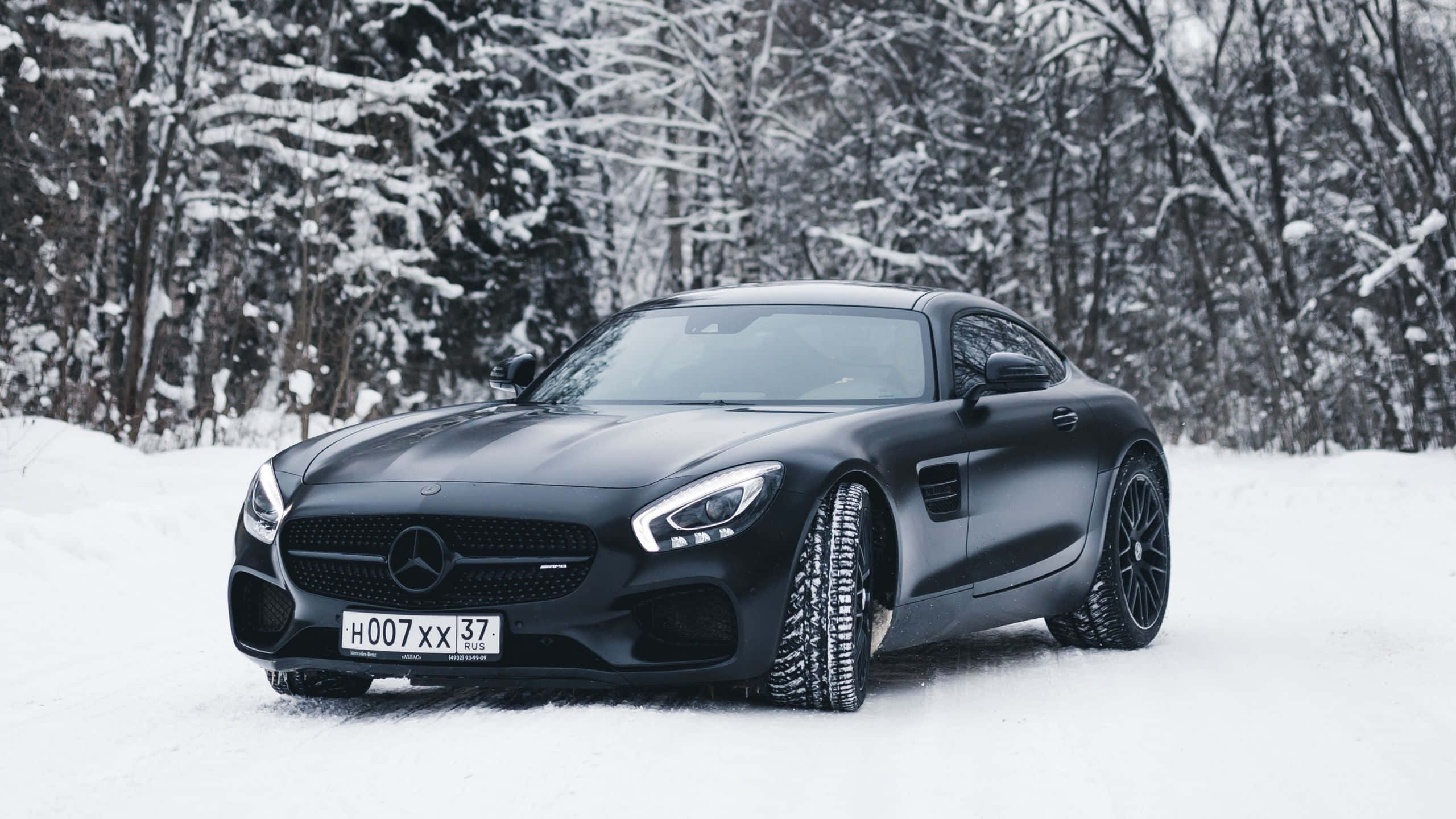 Mercedes 桌布 壁紙 — 一輛時尚的消光黑色 Mercedes-AMG GT 停在深雪中，背景是白雪覆蓋的樹木。