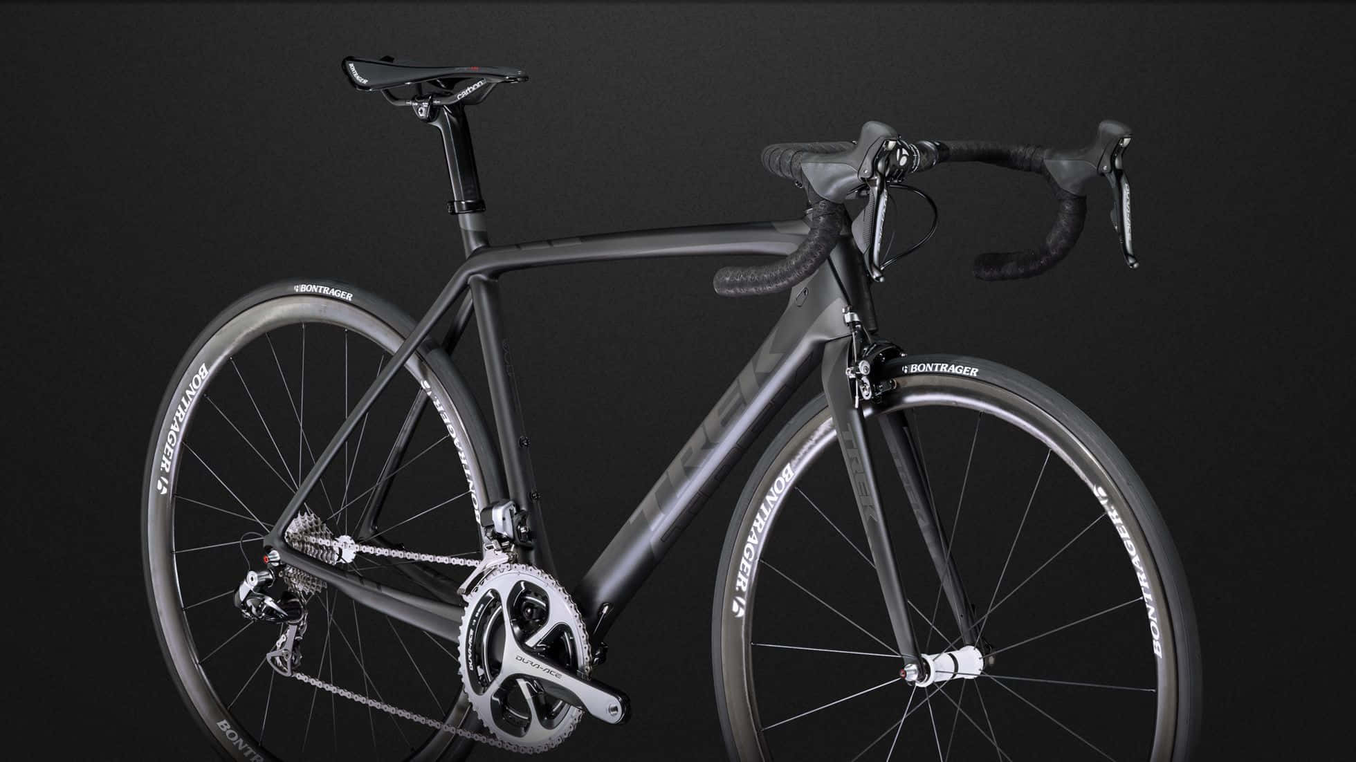 Bikes 桌布 壁紙 — 一輛時尚的消光黑色公路自行車，帶有白色點綴和Bontager輪組，在黑暗的攝影棚背景下蓄勢待發。