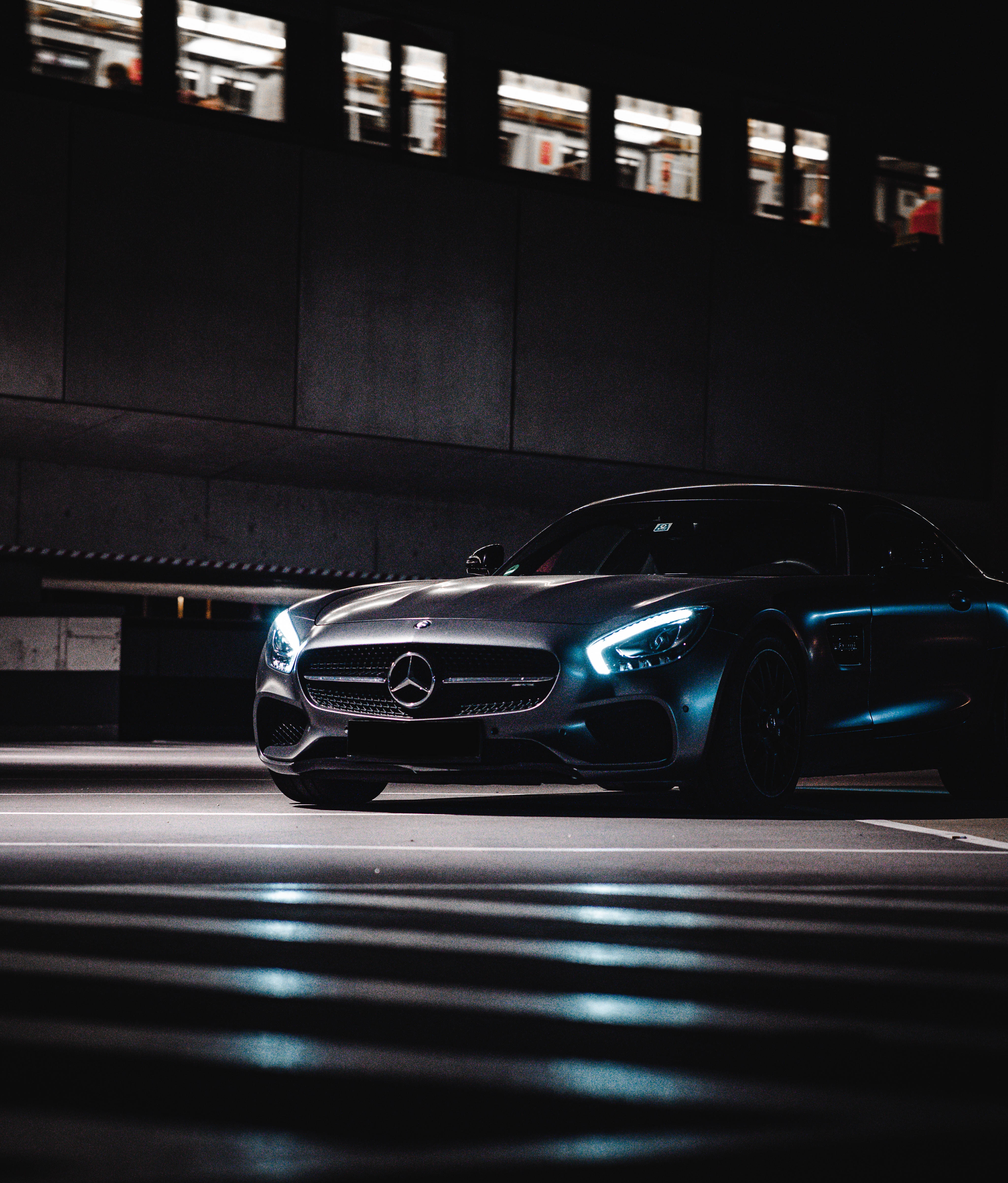 Mercedes 桌布 壁紙 — 一輛時尚的消光黑色梅賽德斯-AMG GT在夜晚停放在混凝土天橋下，車頭燈閃爍，倒映在濕漉漉的路面上。