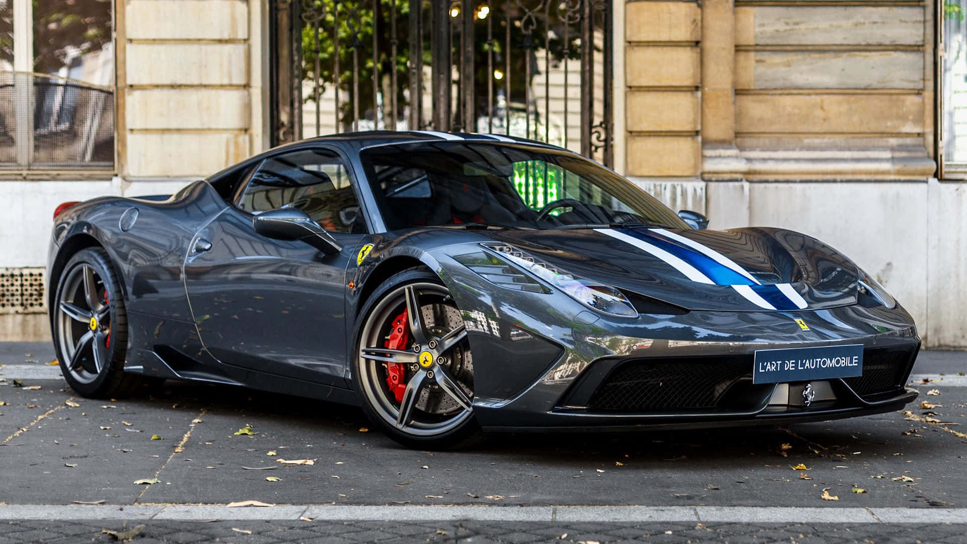 Ferrari 458 Speciale 桌布 壁紙 — 一輛時尚的消光黑色法拉利跑車，帶有藍色賽車條紋，停在歷史建築旁邊的城市街道上。