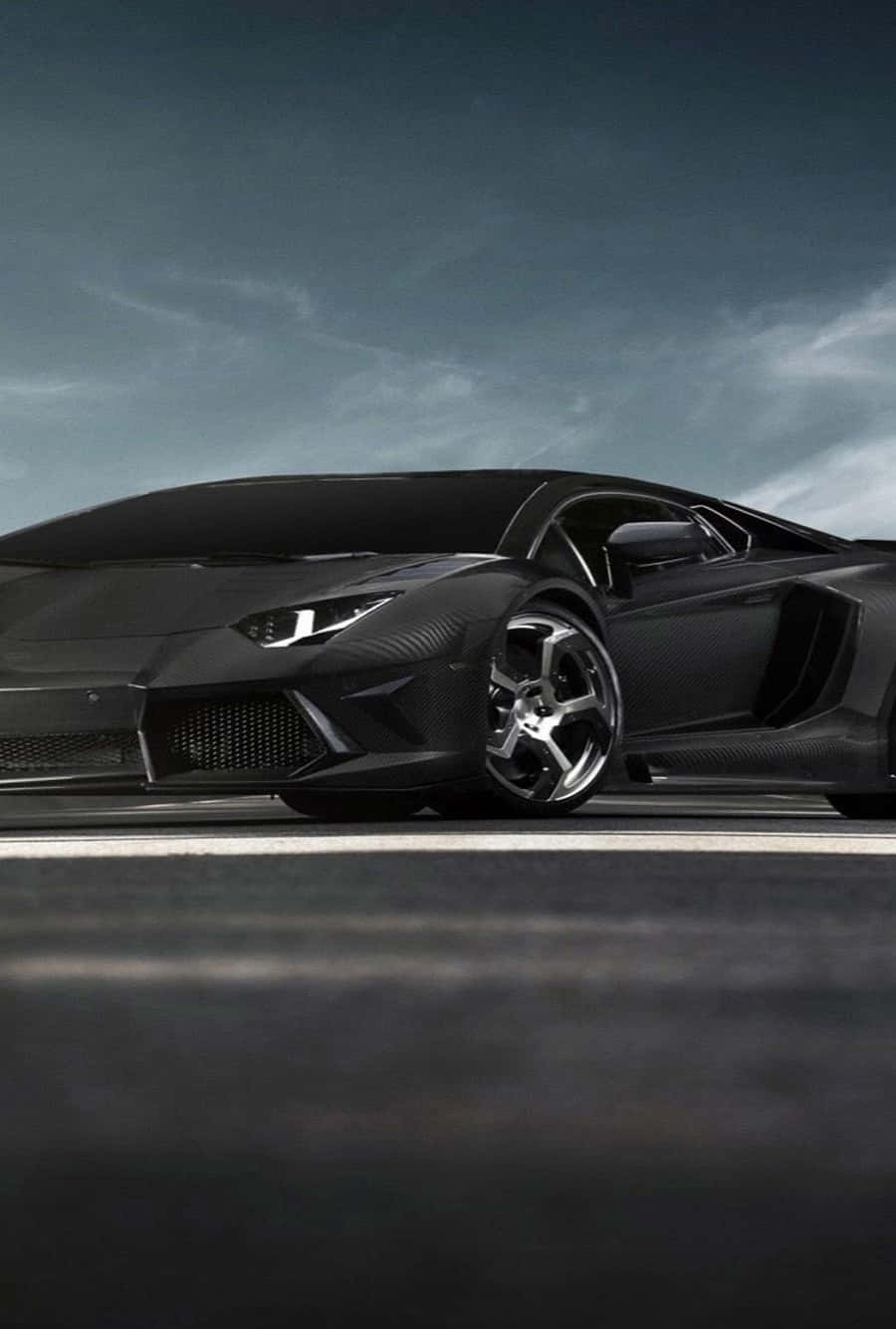 跑車 桌布 壁紙 — 一輛時尚的消光黑色藍寶堅尼 Aventador，配備碳纖維細節和銀色輪圈，停在黑暗的道路上，天空陰沉灰暗。