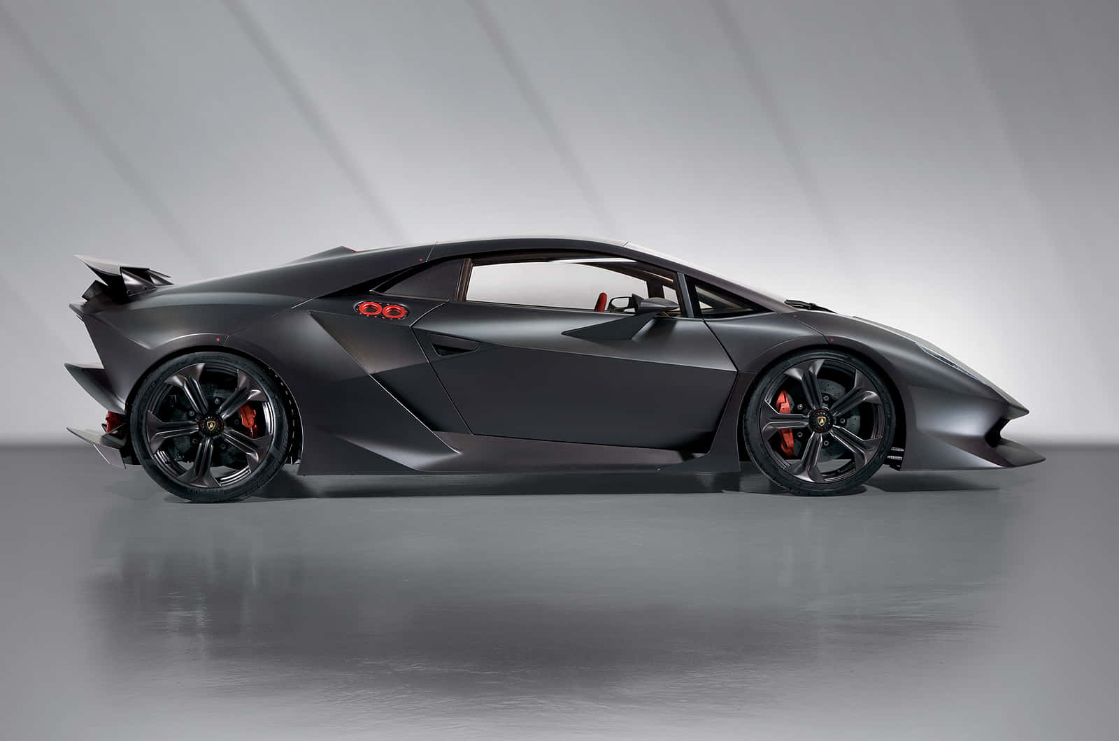 Lamborghini Sesto Elemento 桌布 壁紙 — 一輛時尚的消光黑色藍寶堅尼跑車，帶有紅色點綴和空氣動力學設計，在簡約的工作室中擺拍。