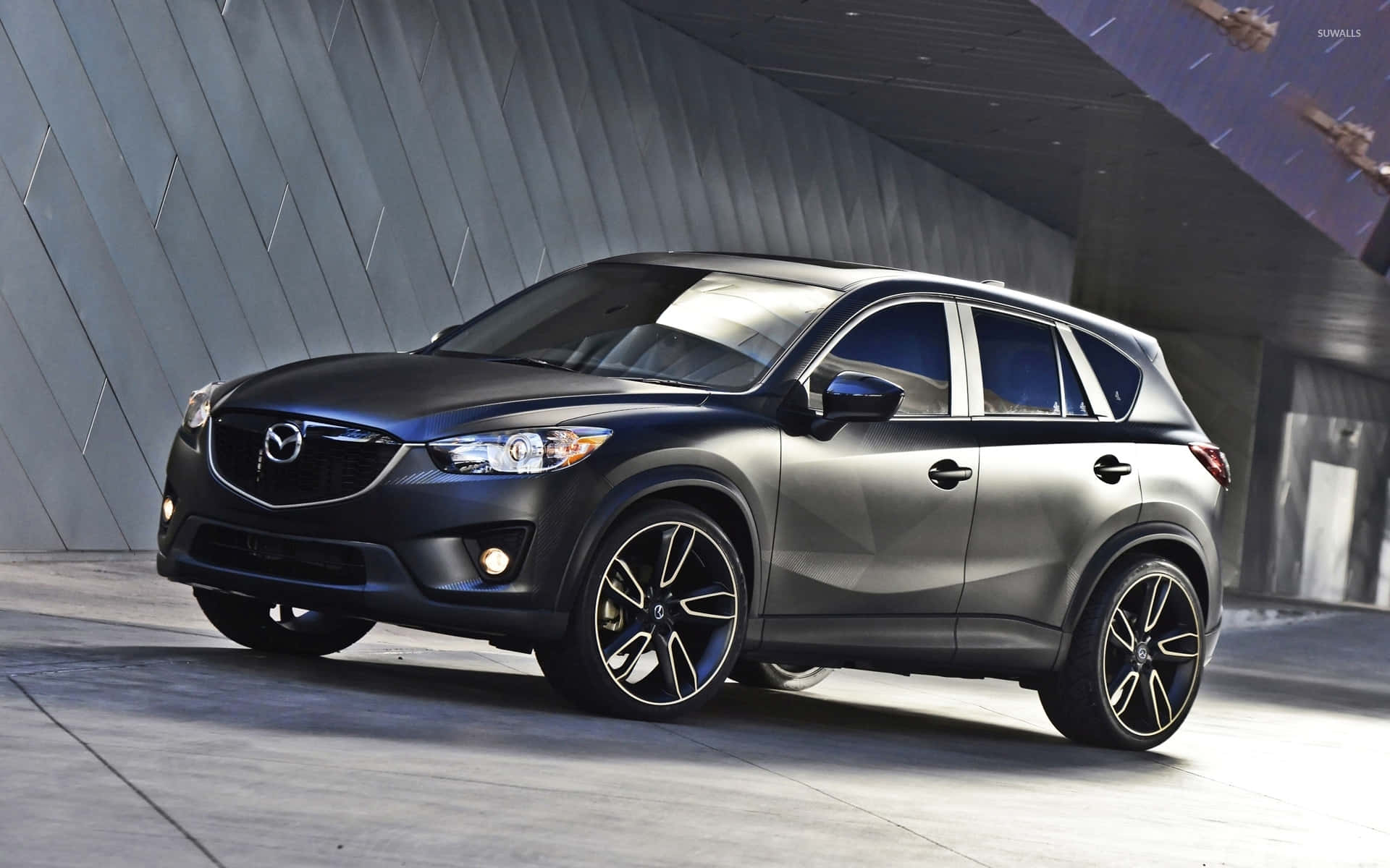 Mazda Cx-5 桌布 壁紙 — 一輛時尚的消光黑色馬自達 CX-5 SUV 配備黑色輪圈，停放在現代角形混凝土結構下。