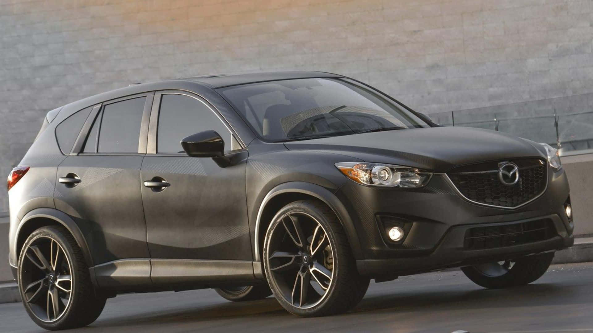 Mazda Cx-5 桌布 壁紙 — 一輛時尚的消光黑色馬自達CX-5 SUV停靠在混凝土牆邊，配備時尚合金輪圈。