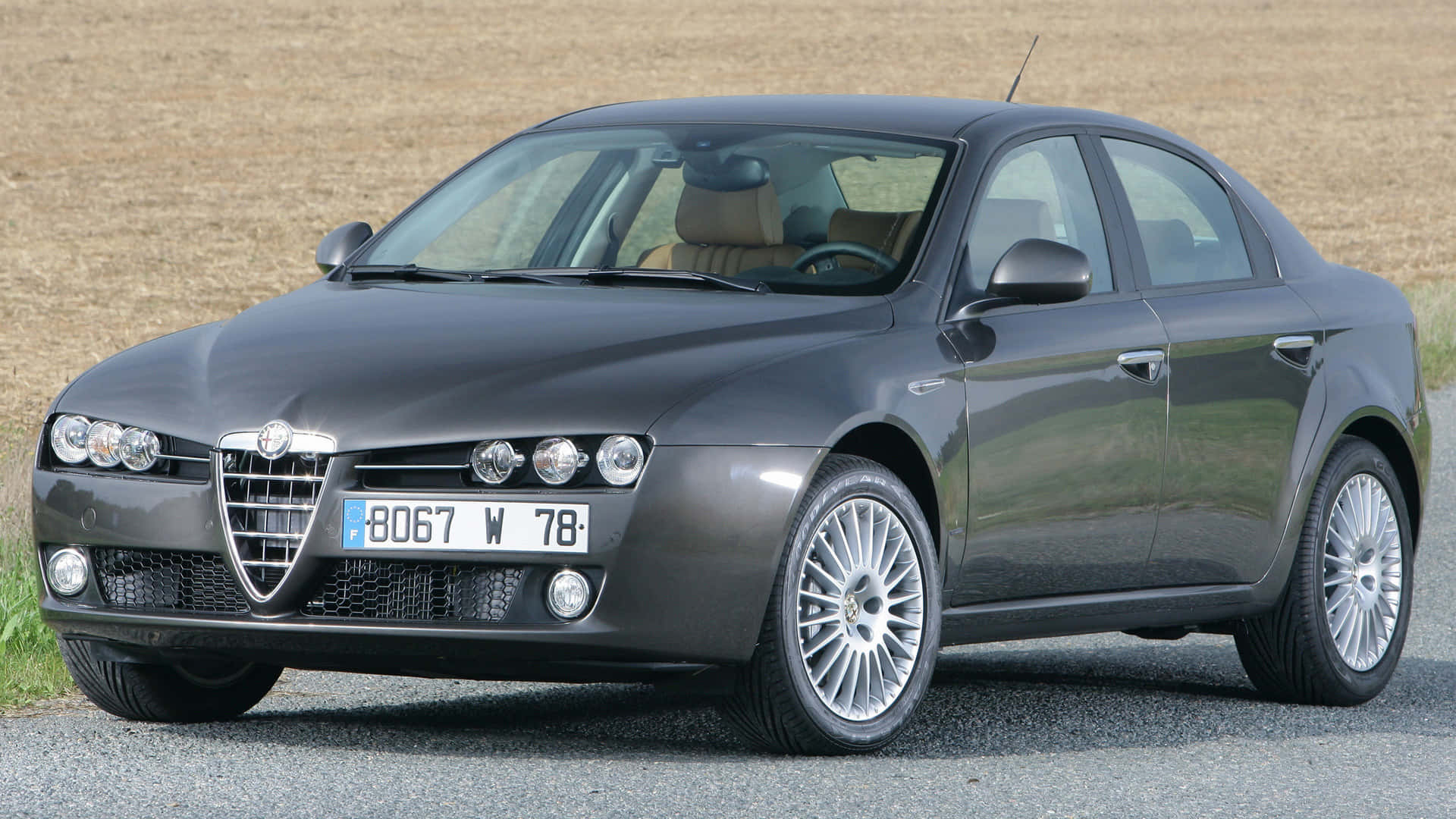 Alfa Romeo 159 桌布 壁紙 — 一輛時尚的深灰色 Alfa Romeo 轎車停在碎石上，後面是乾燥的田野。