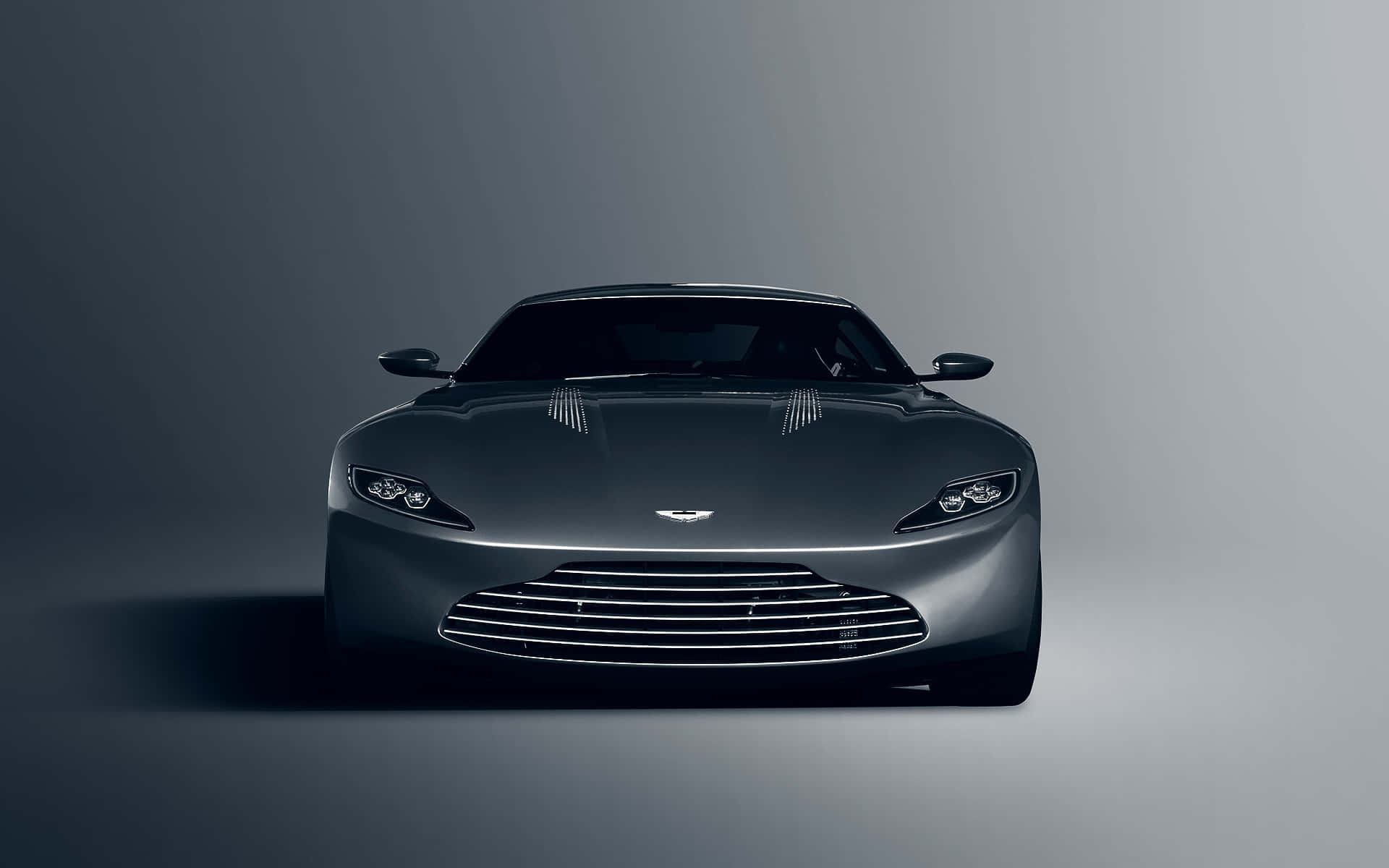 奧斯頓馬丁 桌布 壁紙 — 一輛時尚的深灰色 Aston Martin 跑車在極簡風格的工作室中正面朝前，配有柔和的漸變燈光。
