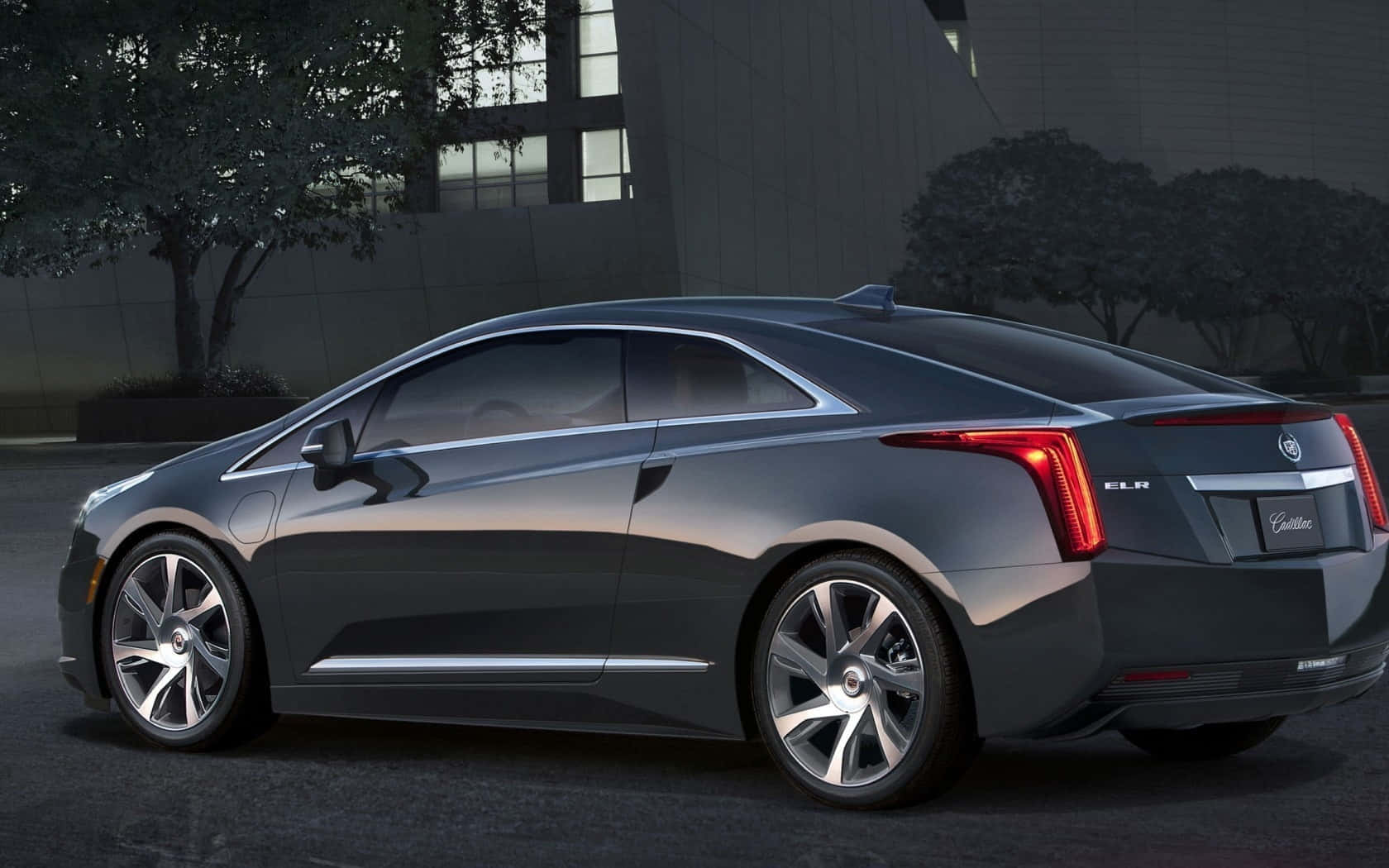 Cadillac Elr 桌布 壁紙 — 一輛時尚的深灰色 Cadillac ELR 電動轎跑車在黃昏時停泊，背景有現代建築和樹木。