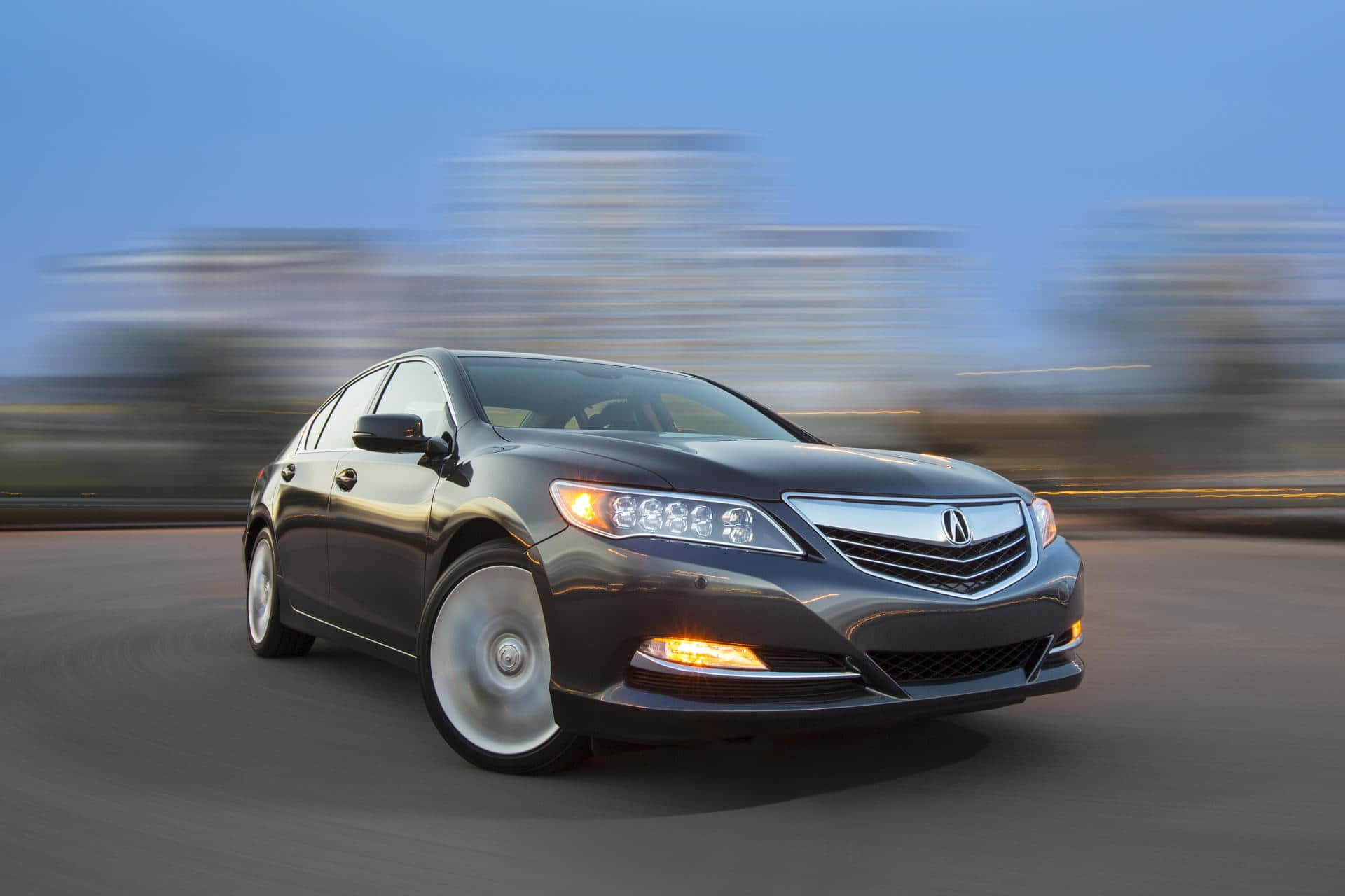 Acura Rlx 桌布 壁紙 — 一輛時尚的深灰色Acura轎車在黃昏時分沿著道路飛馳，背景是模糊的城市景觀。
