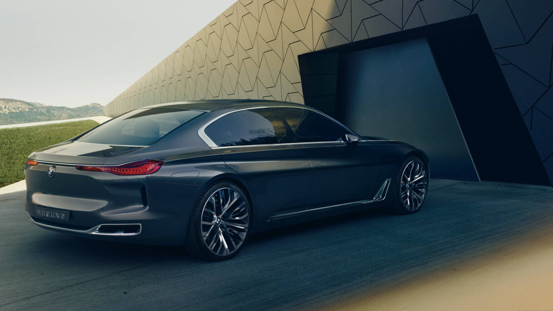 Luxury 桌布 壁紙 — 一輛時尚的深灰色BMW概念車停放在一座現代幾何建築旁邊，背景有山巒。
