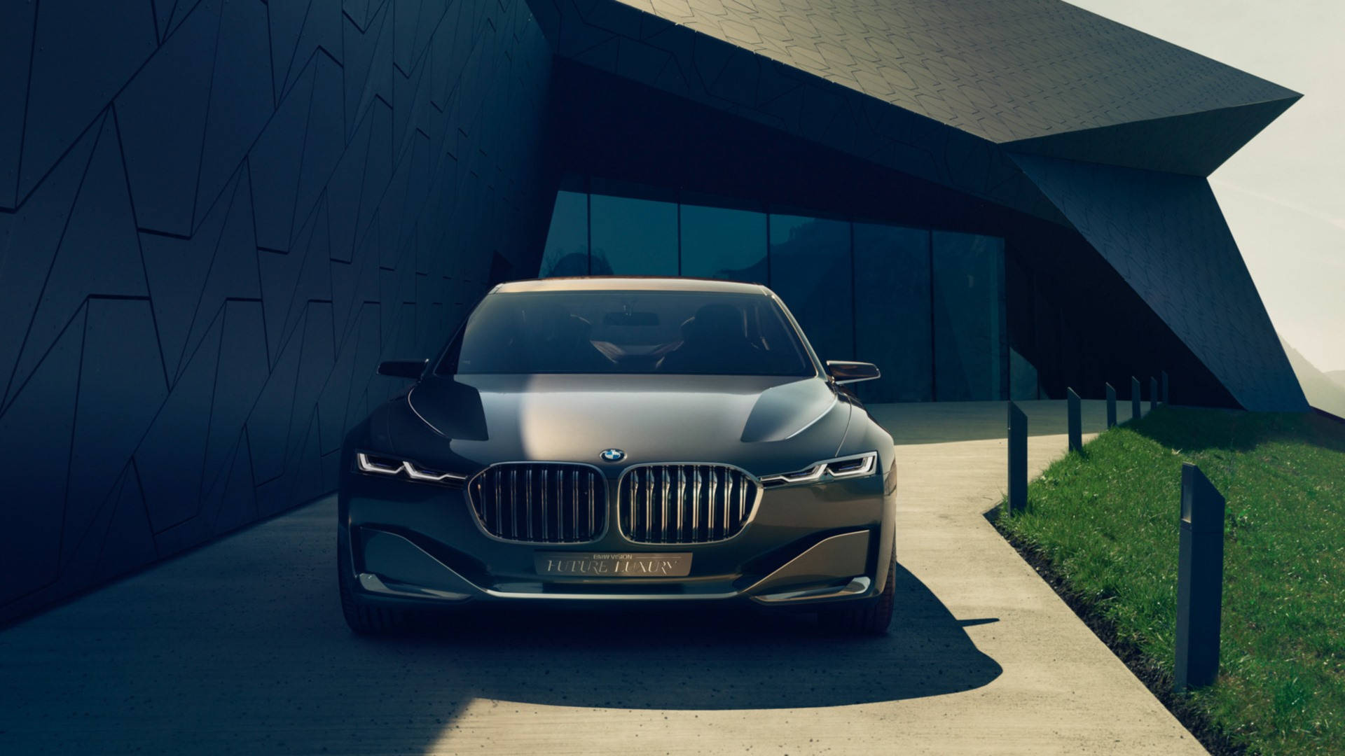 Luxury 桌布 壁紙 — 一輛時尚的深灰色BMW豪華轎車停放在現代幾何牆壁建築和混凝土路旁綠草地的現代棱角建築下。