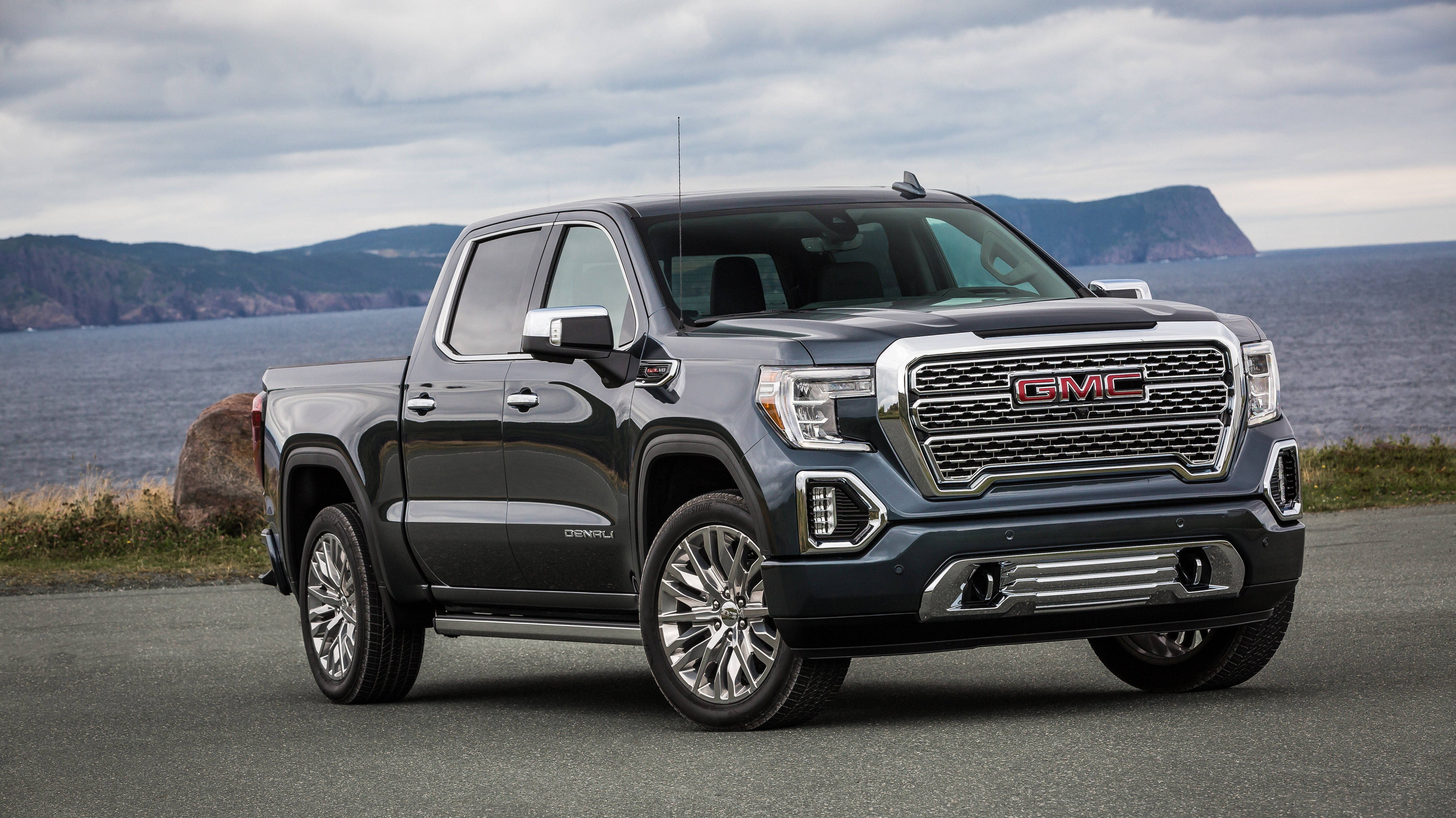 Gmc 桌布 壁紙 — 一輛時尚的深灰色GMC Sierra Denali皮卡車停泊在海岸公路上，背景是海洋和遠處的懸崖，天空多雲。