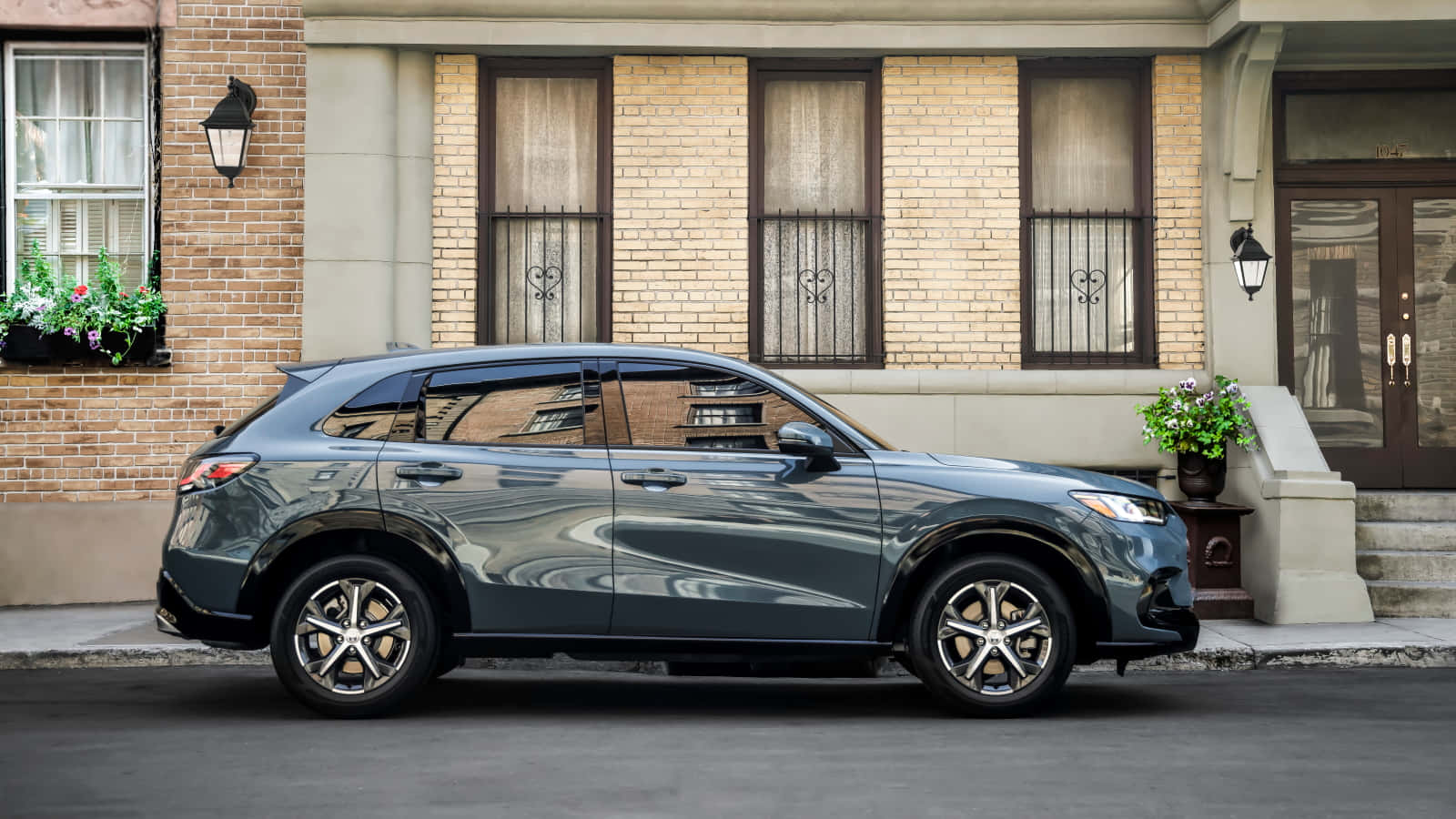 Honda Hr-v 桌布 壁紙 — 一輛時尚的深灰色SUV停放在城市街道上，旁邊是一棟帶有花箱和復古路燈的磚砌建築。