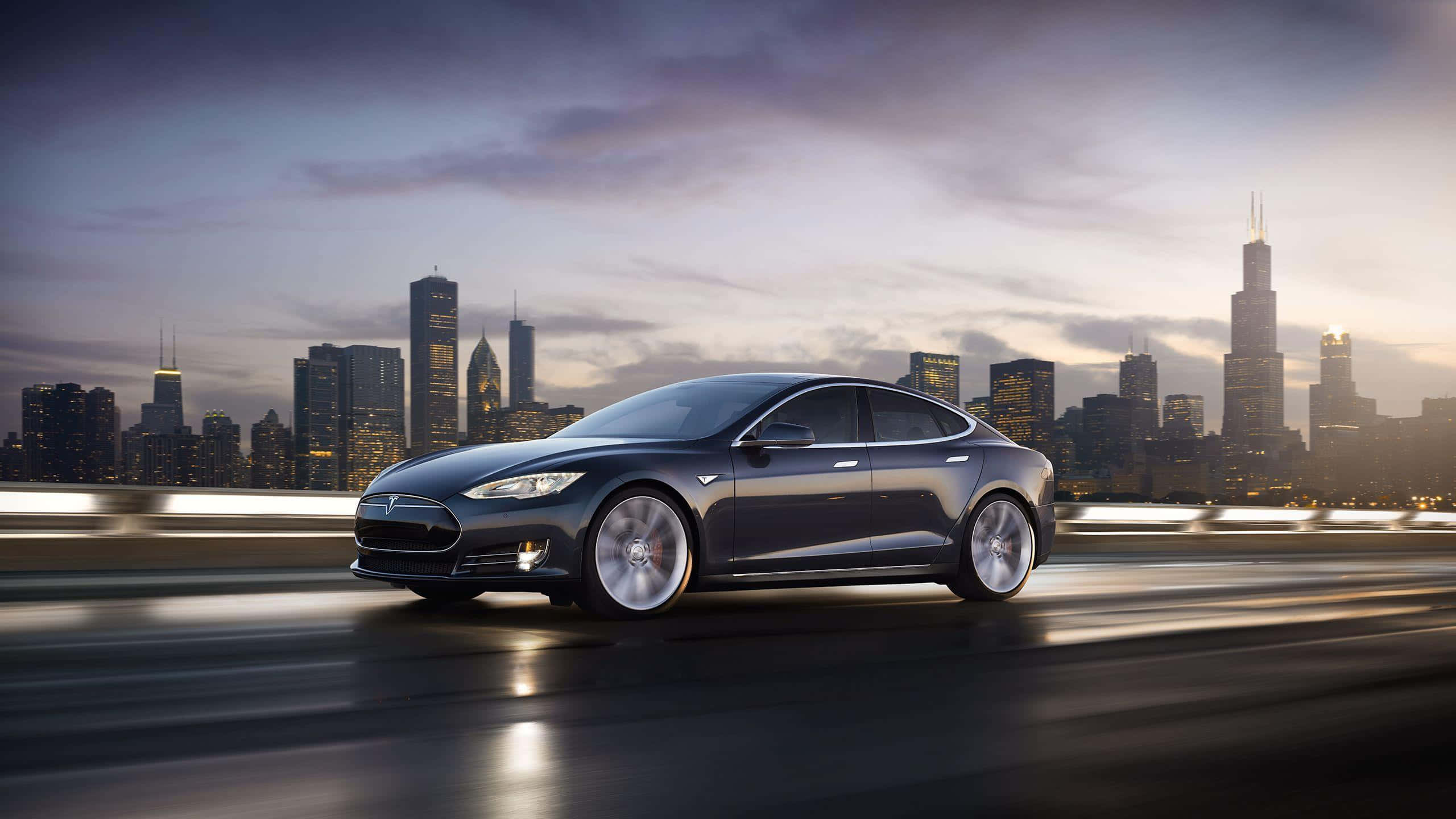 Tesla Model 3 桌布 壁紙 — 一輛時尚的深灰色Tesla Model S在高速公路上奔馳，芝加哥璀璨的天際線在黃昏時分於其後閃耀。