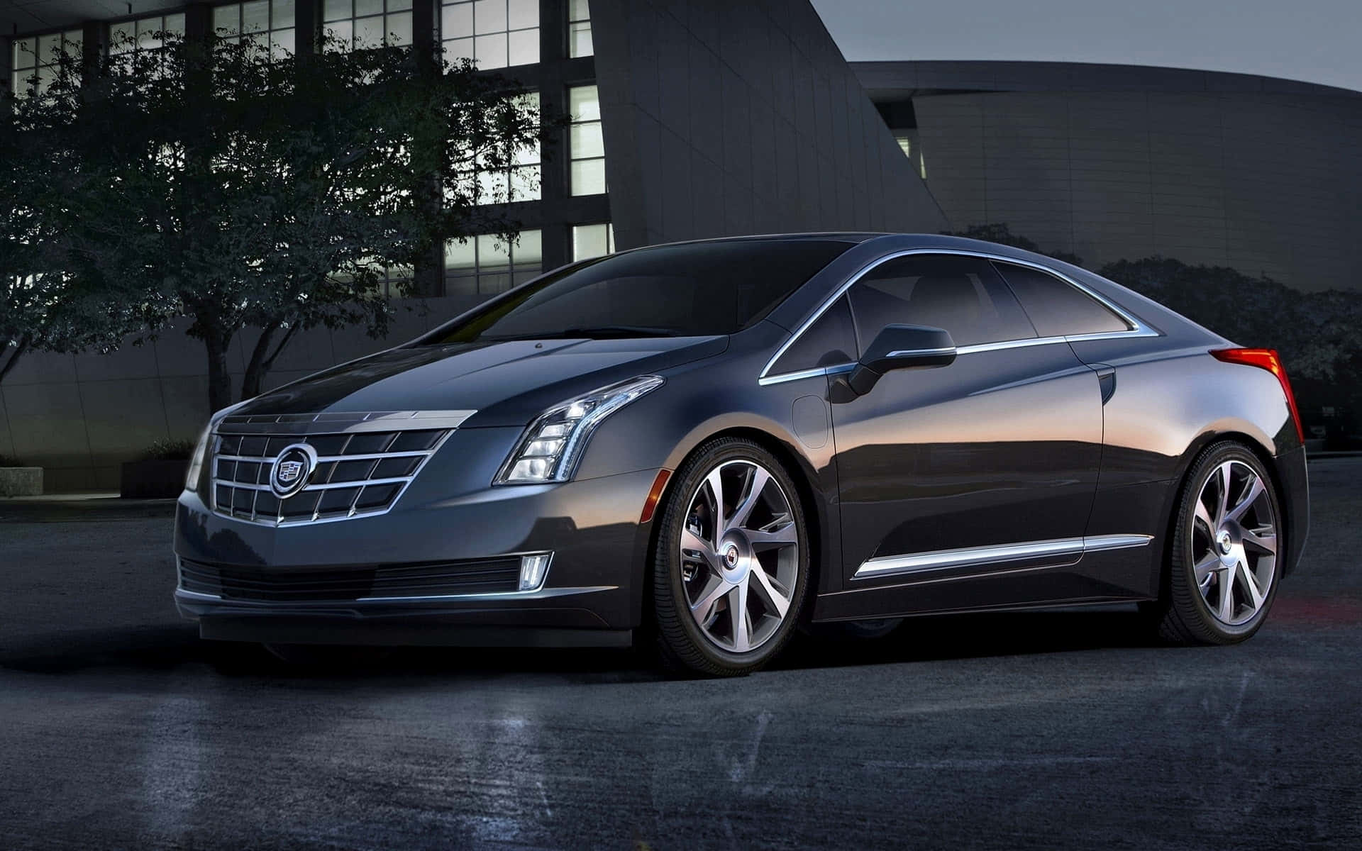 Cadillac Elr 桌布 壁紙 — 一輛時尚的深灰色凱迪拉克ELR轎跑車在暮色燈光下閃耀，以現代建築為背景。