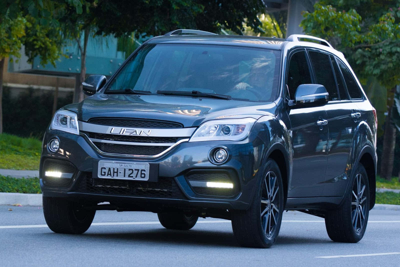 Lifan 桌布 壁紙 — 一輛時尚的深灰色力帆SUV停泊在林蔭大道上，陽光在其拋光表面上閃爍。