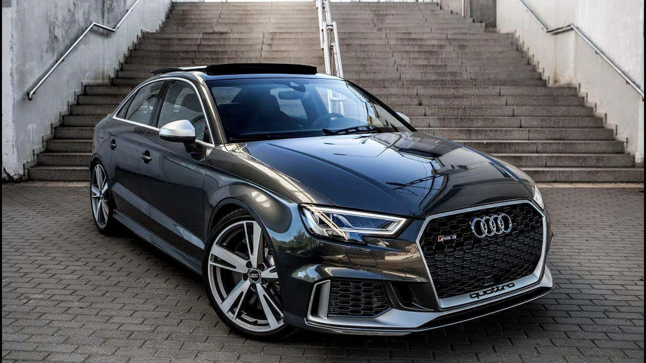 Sedan 桌布 壁紙 — 一輛時尚的深灰色奧迪RS3轎車停放在磚砌廣場上，後方有混凝土階梯聳立。
