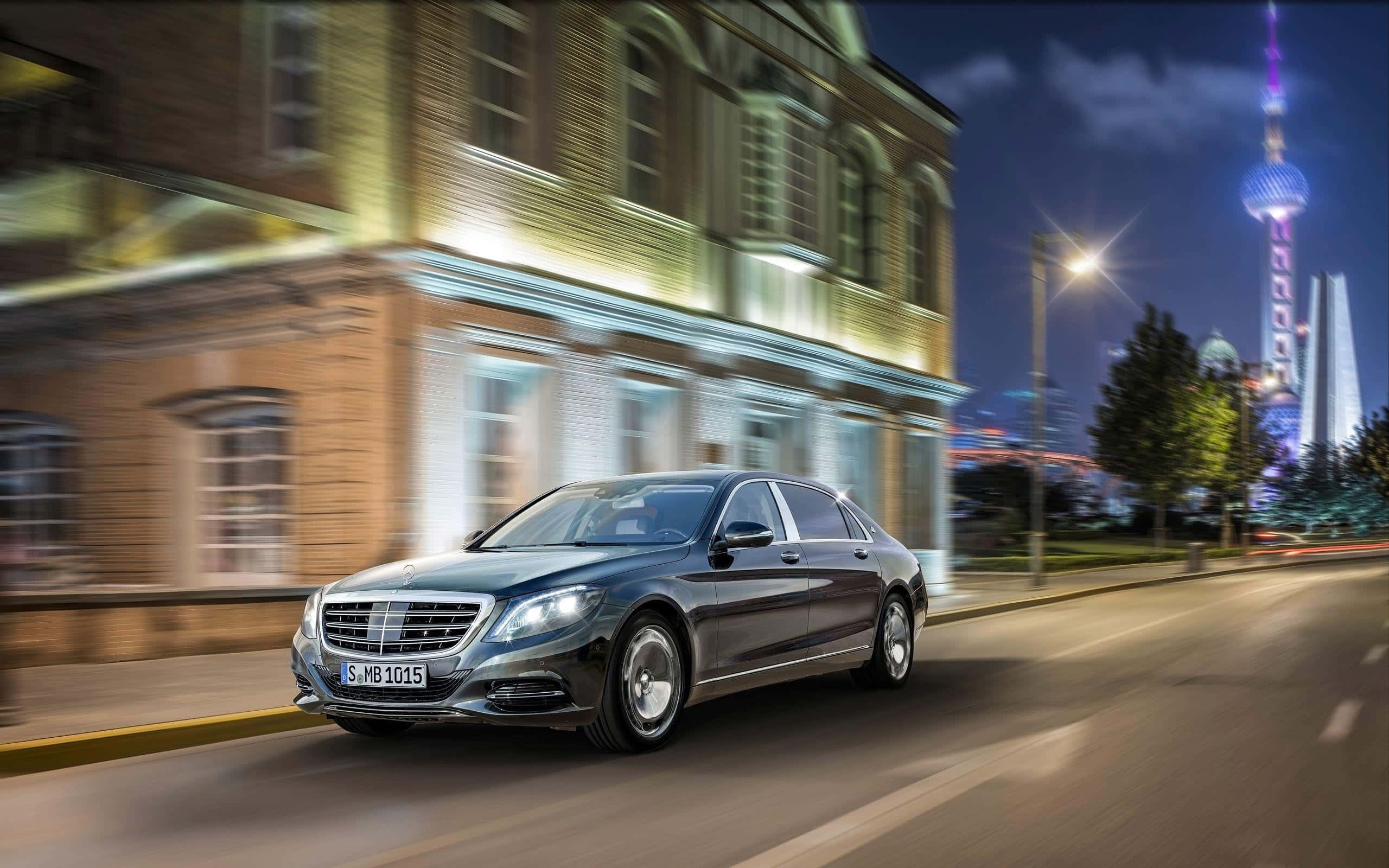 Maybach 桌布 壁紙 — 一輛時尚的深灰色梅賽德斯-奔馳S級轎車在充滿活力的夜間城市景觀中疾馳，帶有模糊的動感和燈火通明的摩天大樓。