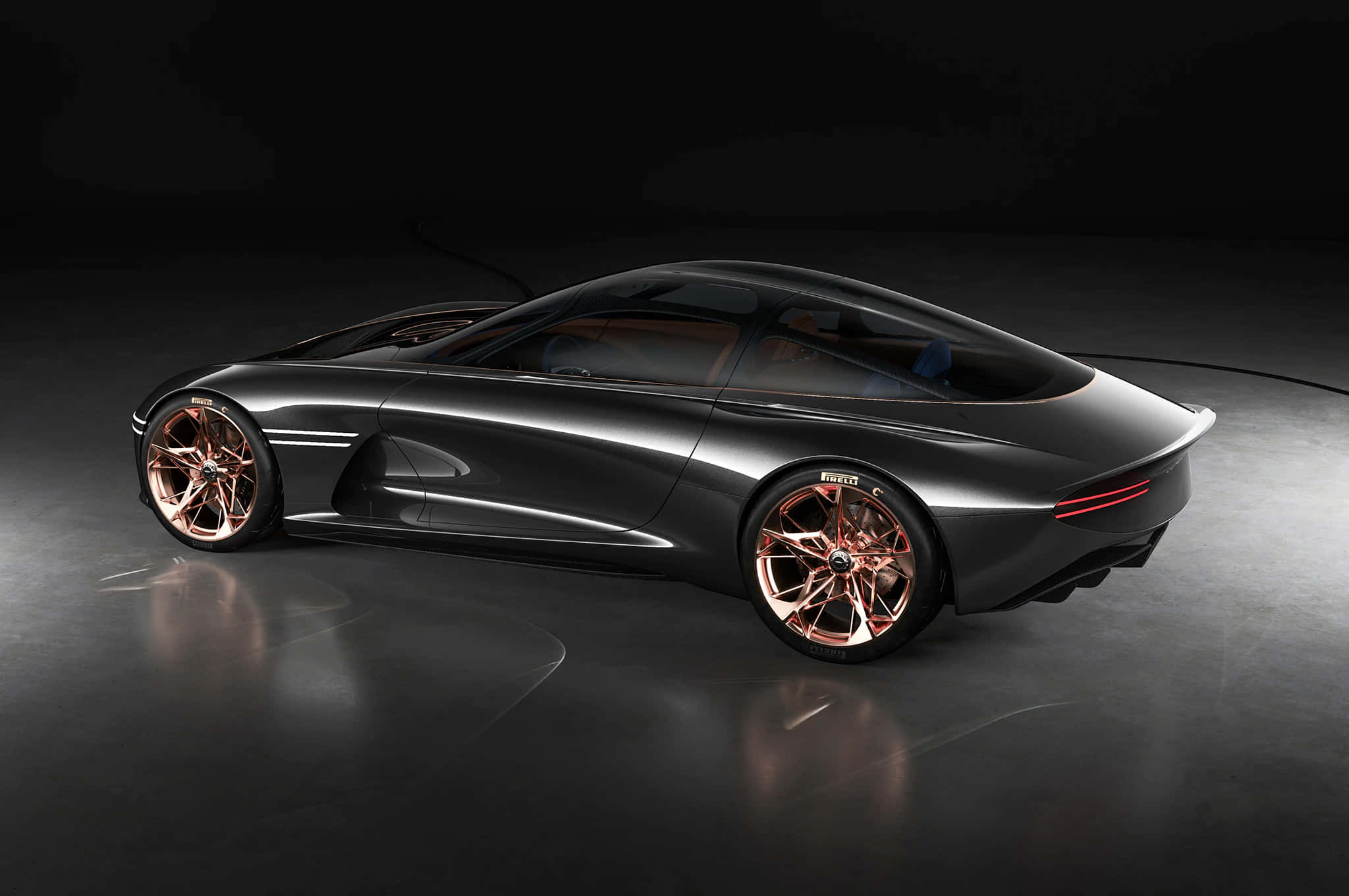 Genesis Essentia 桌布 壁紙 — 一輛時尚的深灰色概念車，配備銅色輪圈，在攝影棚燈光下於反光地板上閃耀。