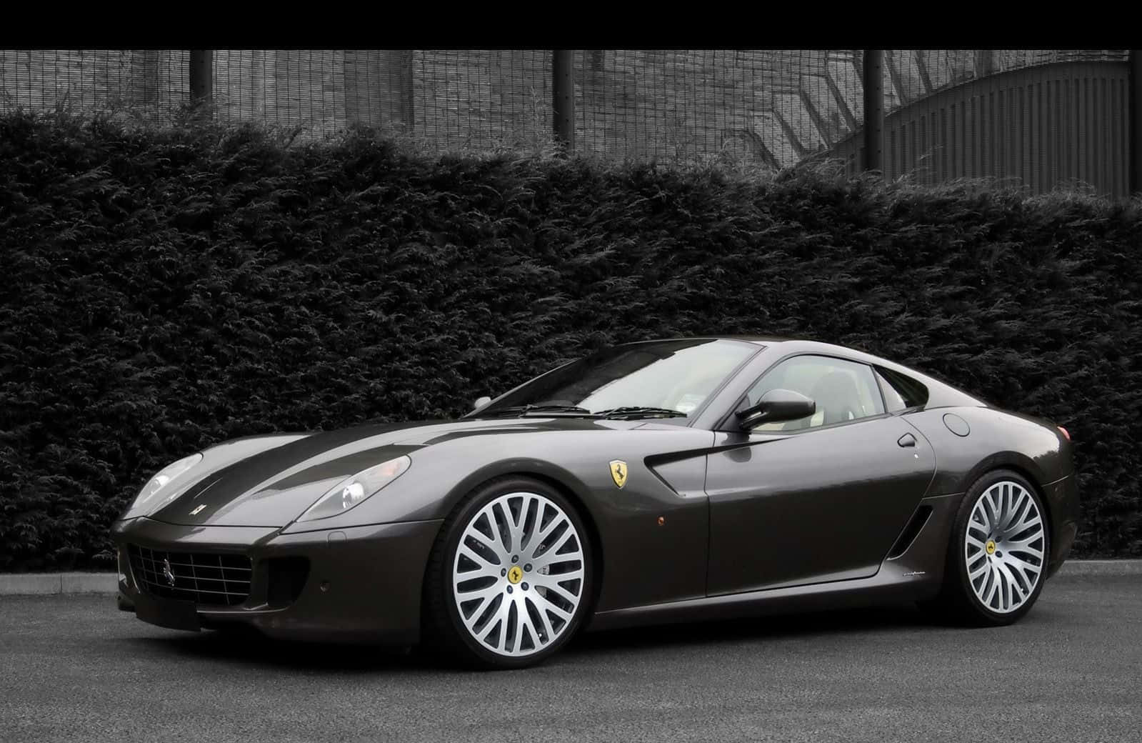 Ferrari 599 Gtb Fiorano 桌布 壁紙 — 一輛時尚的深灰色法拉利跑車停在瀝青路上，背景是茂密的樹籬和圍欄。