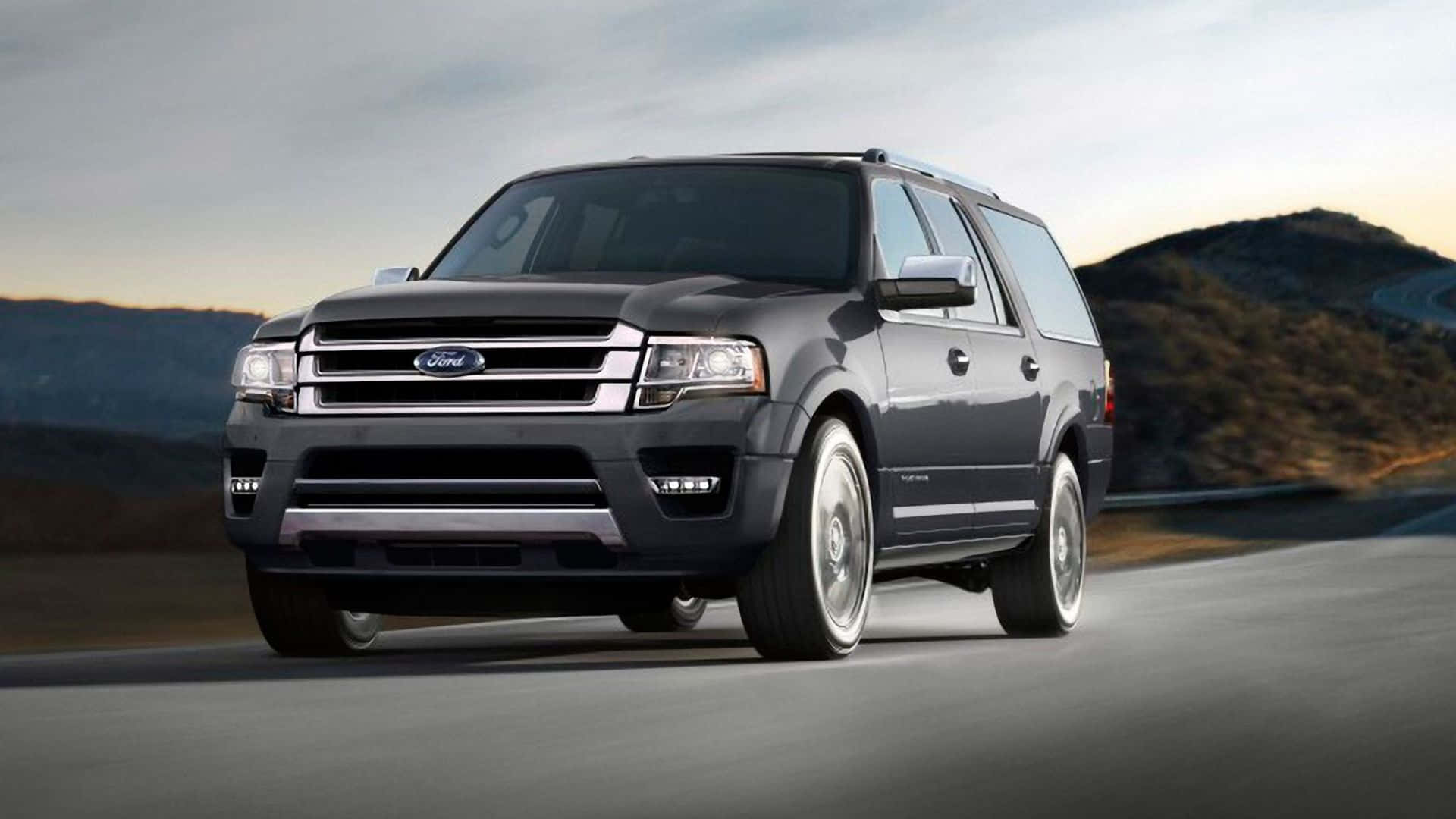 Ford Expedition 桌布 壁紙 — 一輛時尚的深灰色福特 Expedition SUV 在日落時分沿著蜿蜒的山路行駛，沐浴在溫暖的金色光芒中。