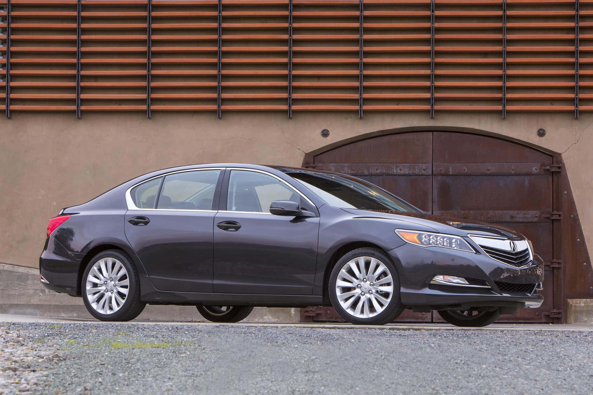 Acura Rlx 桌布 壁紙 — 一輛時尚的深灰色轎車停在一棟質樸的建築前，建築有木條牆和拱形金屬門。