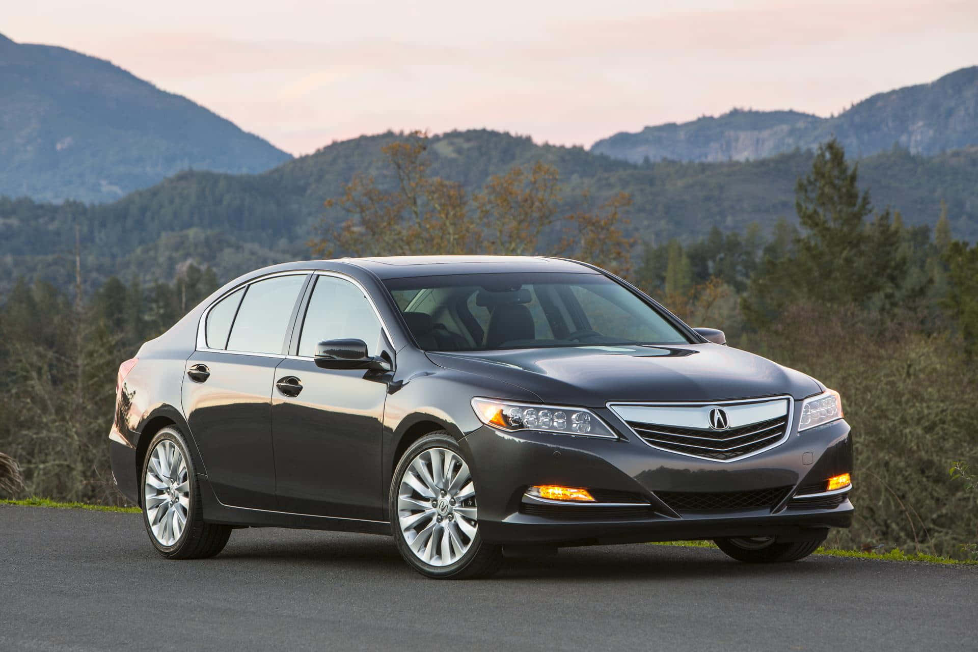 Acura Rlx 桌布 壁紙 — 一輛時尚的深灰色轎車停泊在日落時分有山脈和樹木背景的道路上。