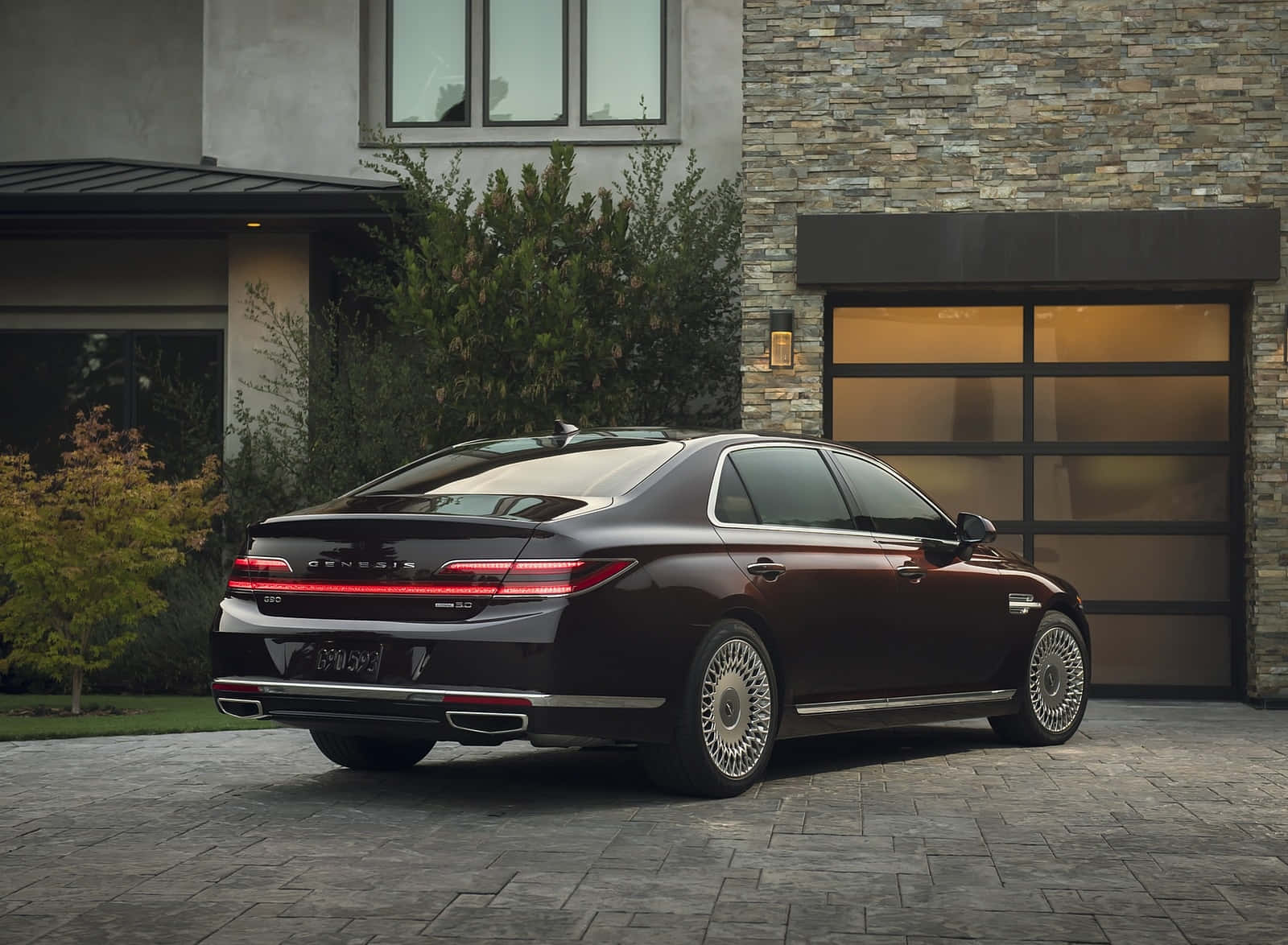Genesis G90 桌布 壁紙 — 一輛時尚的深紅色Genesis G90豪華轎車停放在現代石頭和玻璃屋前的石頭車道上。