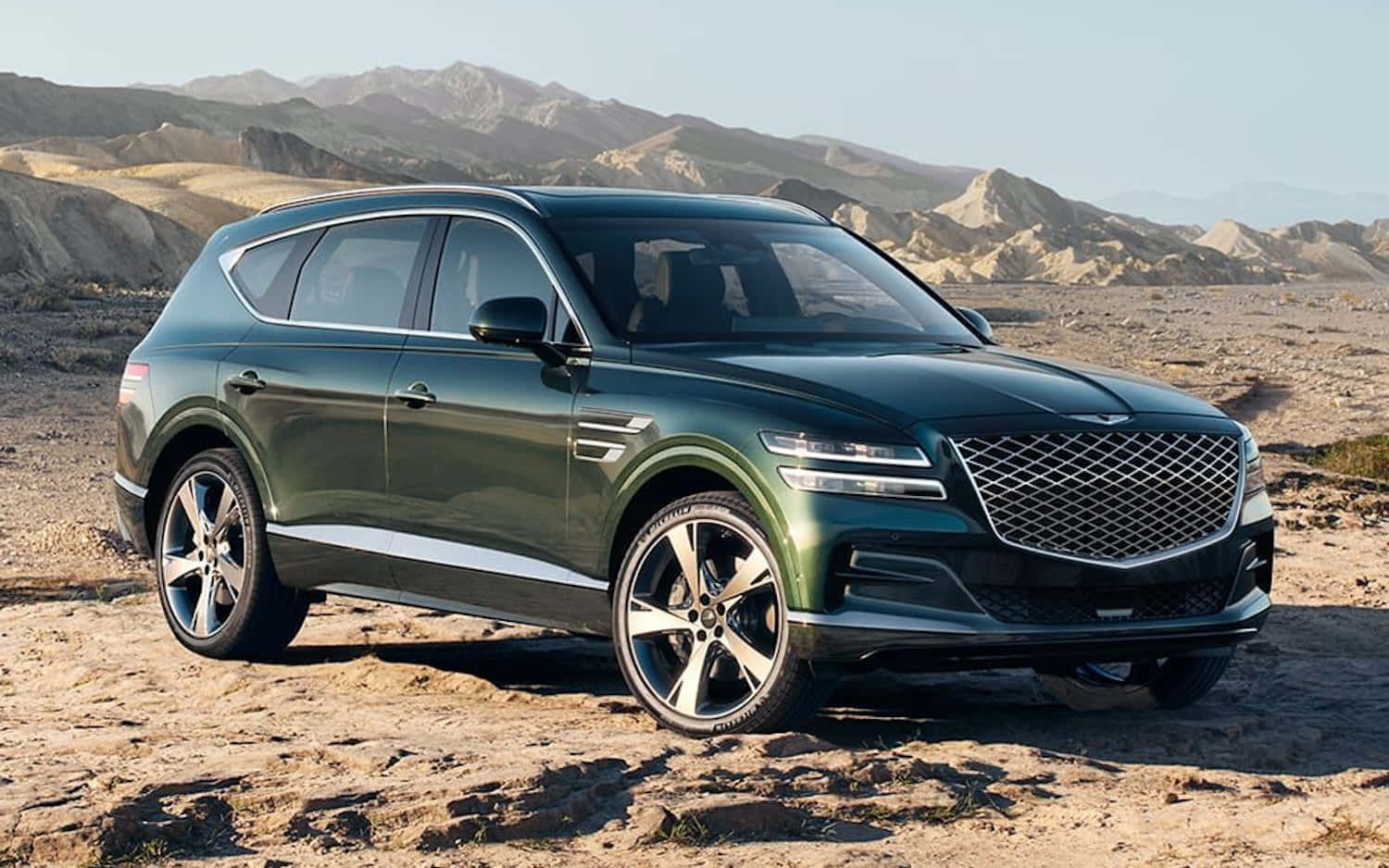 Genesis Gv80 桌布 壁紙 — 一輛時尚的深綠色 Genesis GV80 SUV 停泊在岩石沙漠地形上，背景是崎嶇的山脈，天空晴朗。