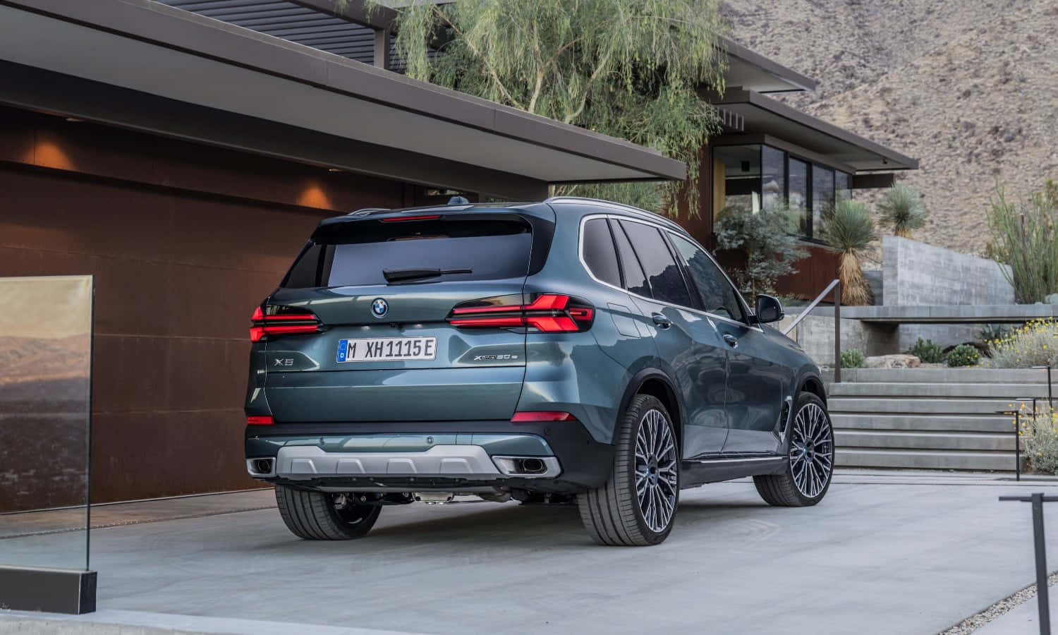 Bmw X5 桌布 壁紙 — 一輛時尚的深綠色BMW X5 xDrive45e SUV停在帶有沙漠景觀的現代房屋前。