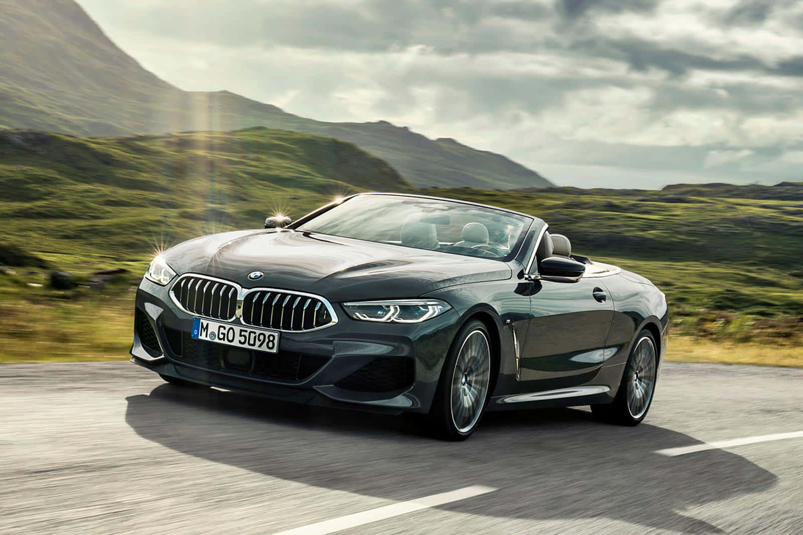 Bmw 8 Series 桌布 壁紙 — 一輛時尚的深綠色BMW敞篷車在陰天下行駛在蜿蜒的山路上。