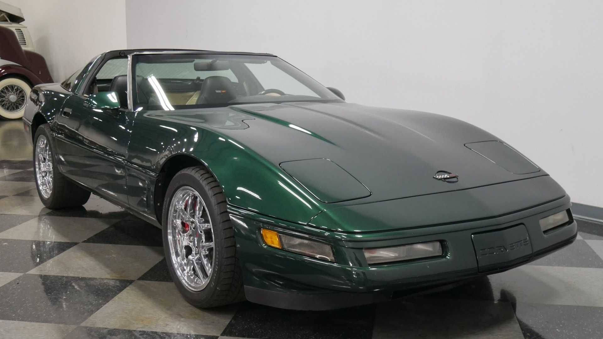 corvette 桌布 壁紙 — 一輛時尚的深綠色Corvette跑車在明亮的燈光下，在潔淨的室內展廳的格子地板上閃閃發光。