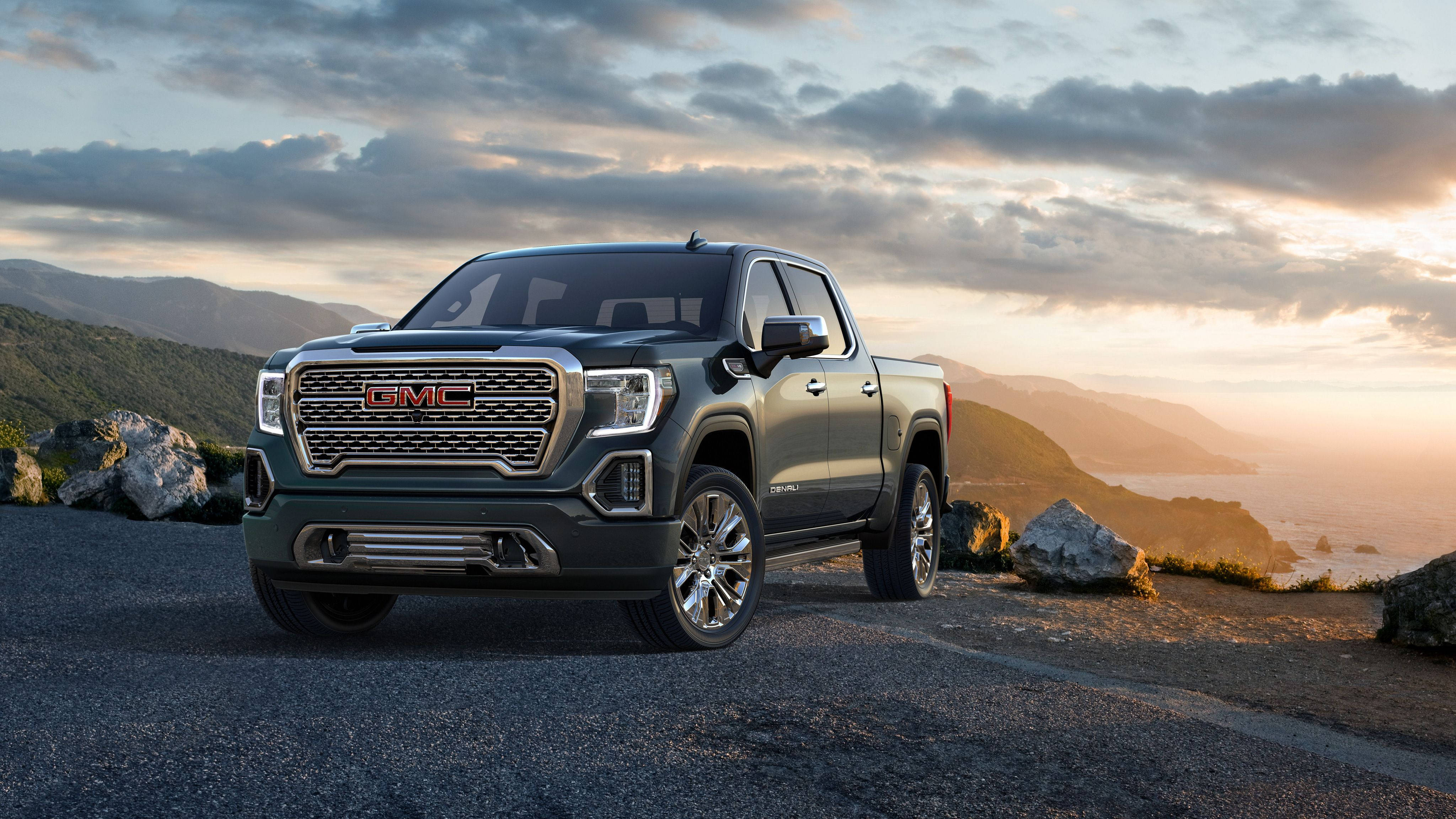 Gmc 桌布 壁紙 — 一輛時尚的深綠色GMC Sierra皮卡車停在日落時分的海岸懸崖上，背景有山脈和海洋。