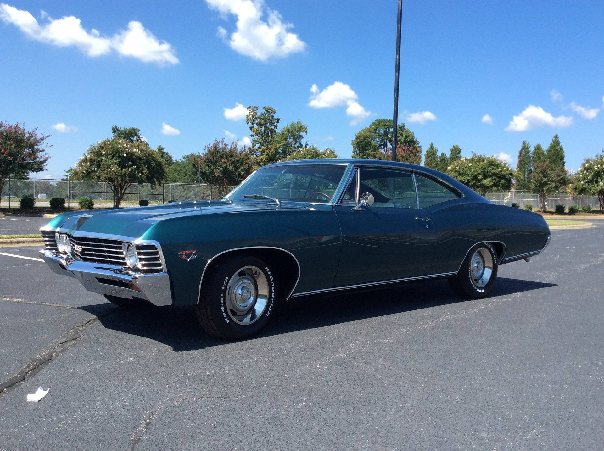 chevrolet impala 1967 桌布 壁紙 — 一輛時尚的深綠色經典肌肉車在晴朗藍天下陽光普照的停車場中閃閃發光。