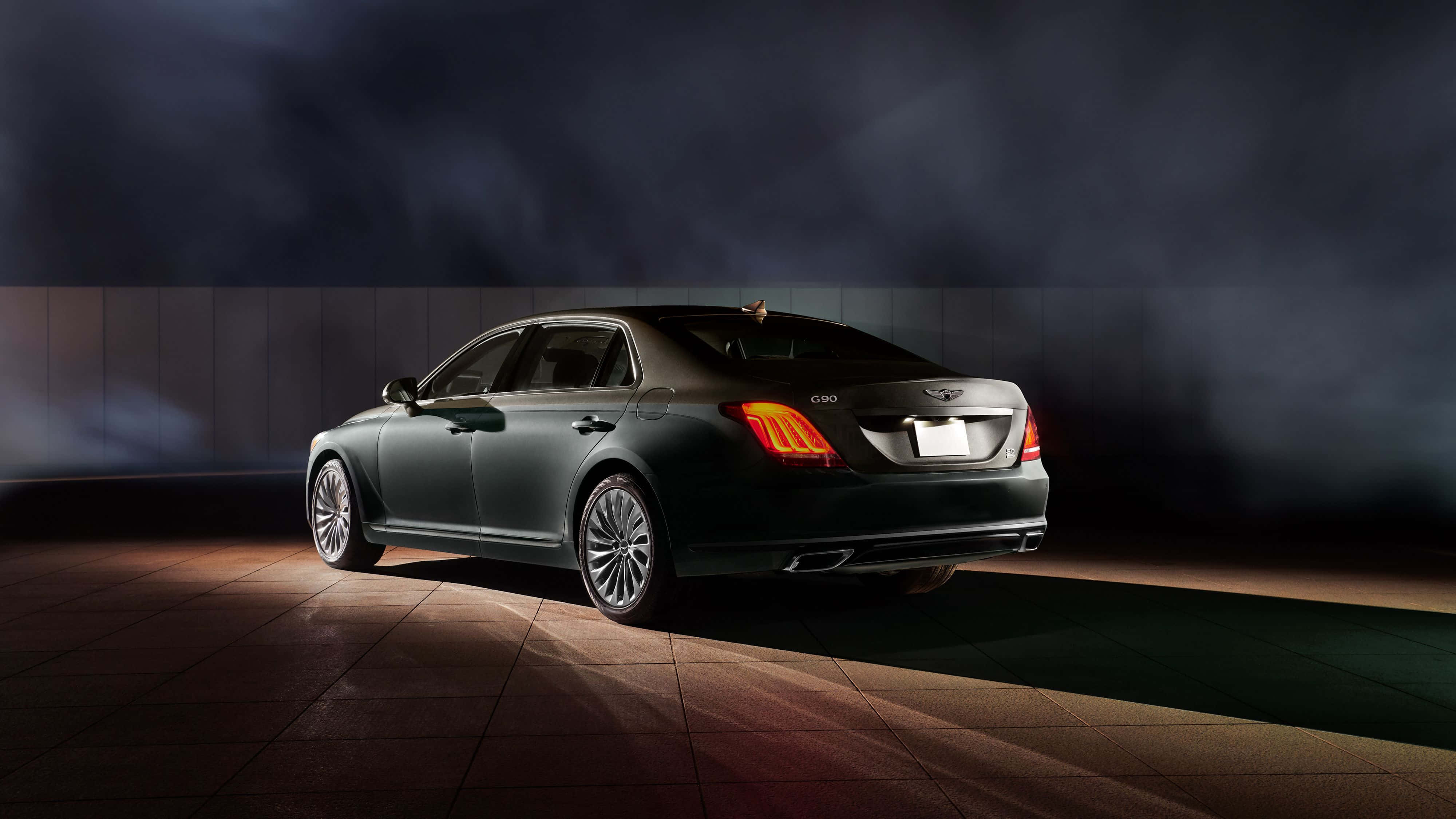 Genesis G90 桌布 壁紙 — 一輛時尚的深綠色豪華轎車在煙霧瀰漫的黑暗背景下，在戲劇性的聚光燈下閃耀。