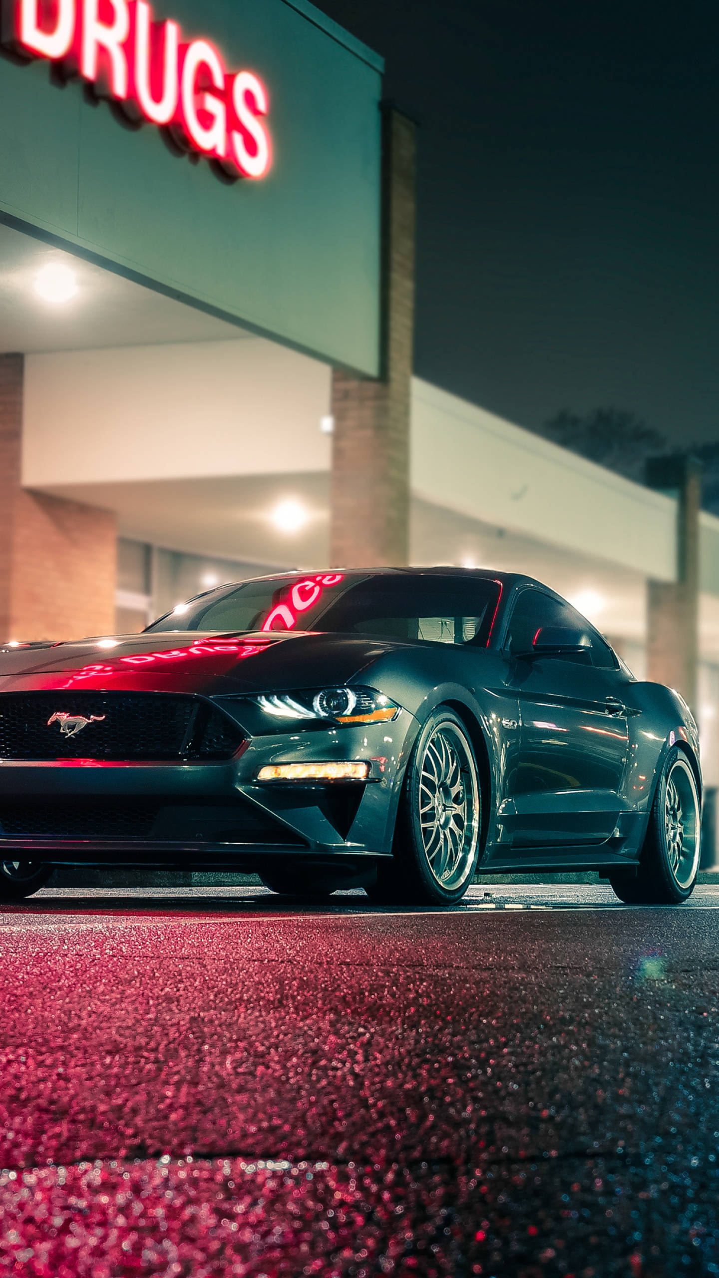 Cool Mustang 桌布 壁紙 — 一輛時尚的深綠色野馬跑車在夜間藥局前的霓虹燈下閃閃發光。