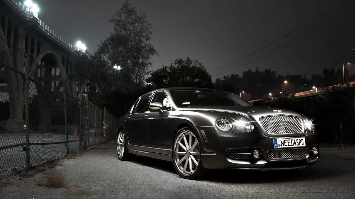 1366x768 Bentley 桌布 壁紙 — 一輛時尚的深色賓利轎車在夜間橋下停泊，在街燈下閃閃發光。