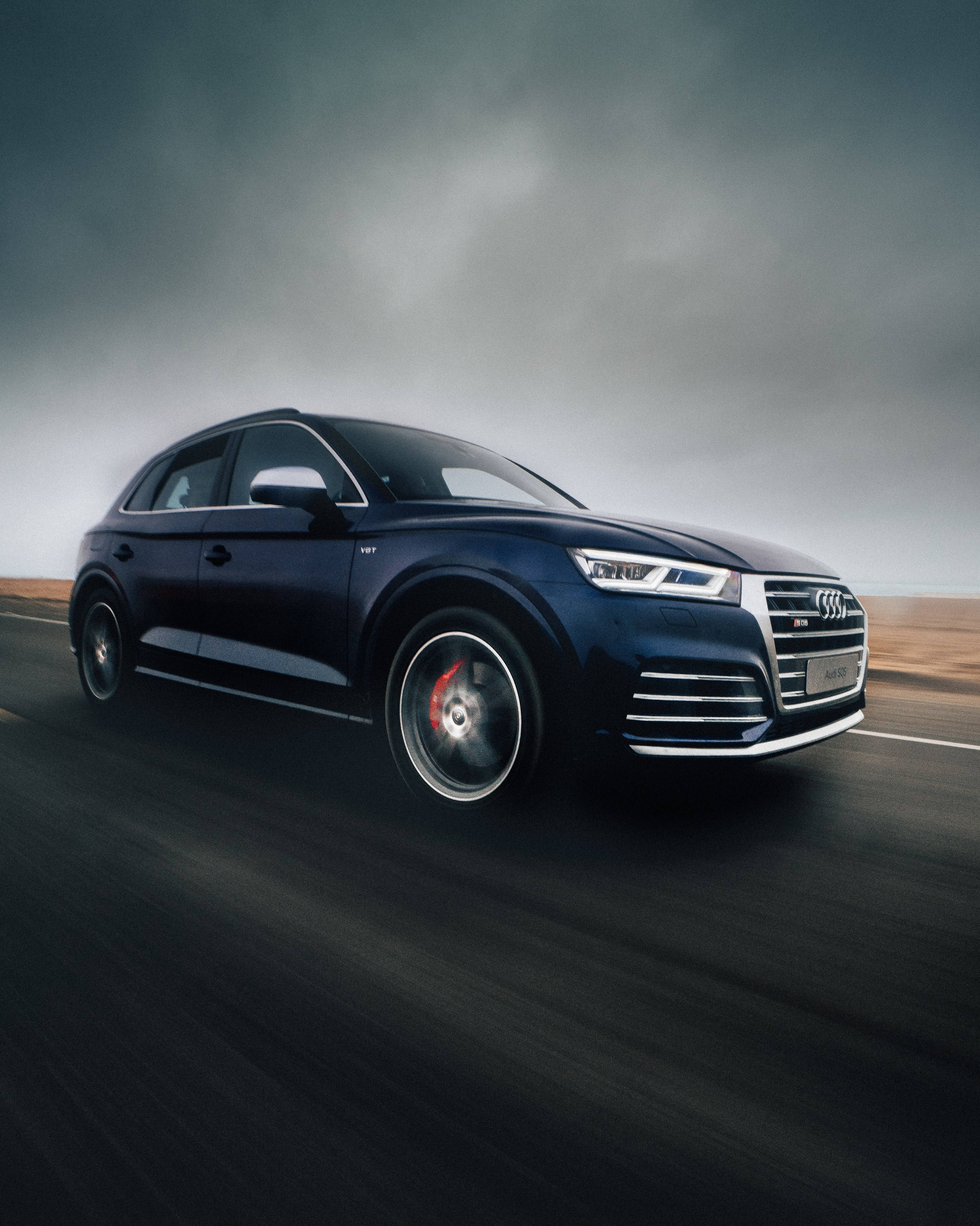 奧迪 桌布 壁紙 — 一輛時尚的深藍色 Audi SQ5 SUV 在潮濕的道路上疾馳，天空陰沉多雲，帶有模糊的動感。