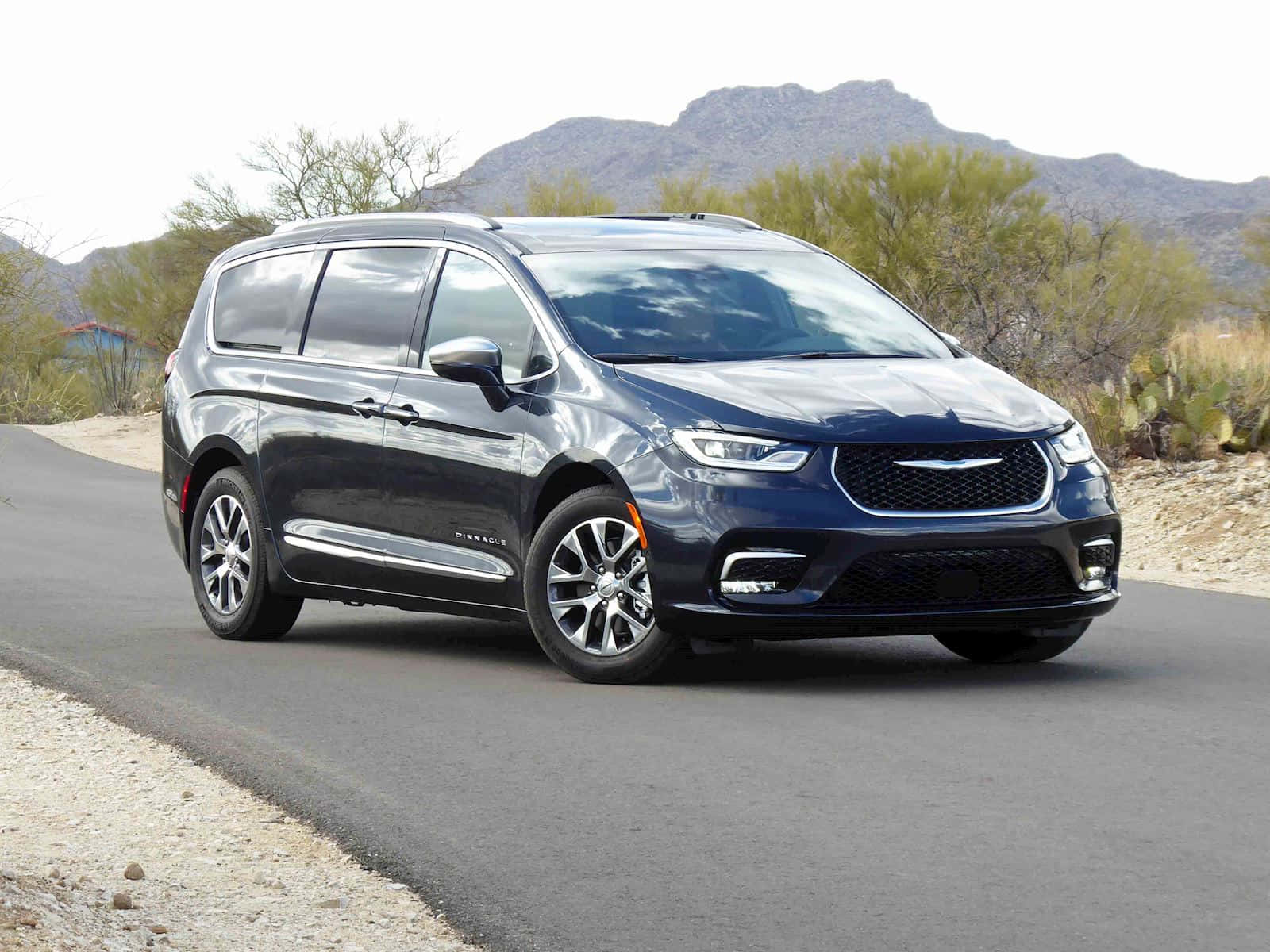 Chrysler Pacifica 桌布 壁紙 — 一輛時尚的深藍色 Chrysler Pacifica 小型貨車在沙漠公路上行駛，背景有山脈和仙人掌。