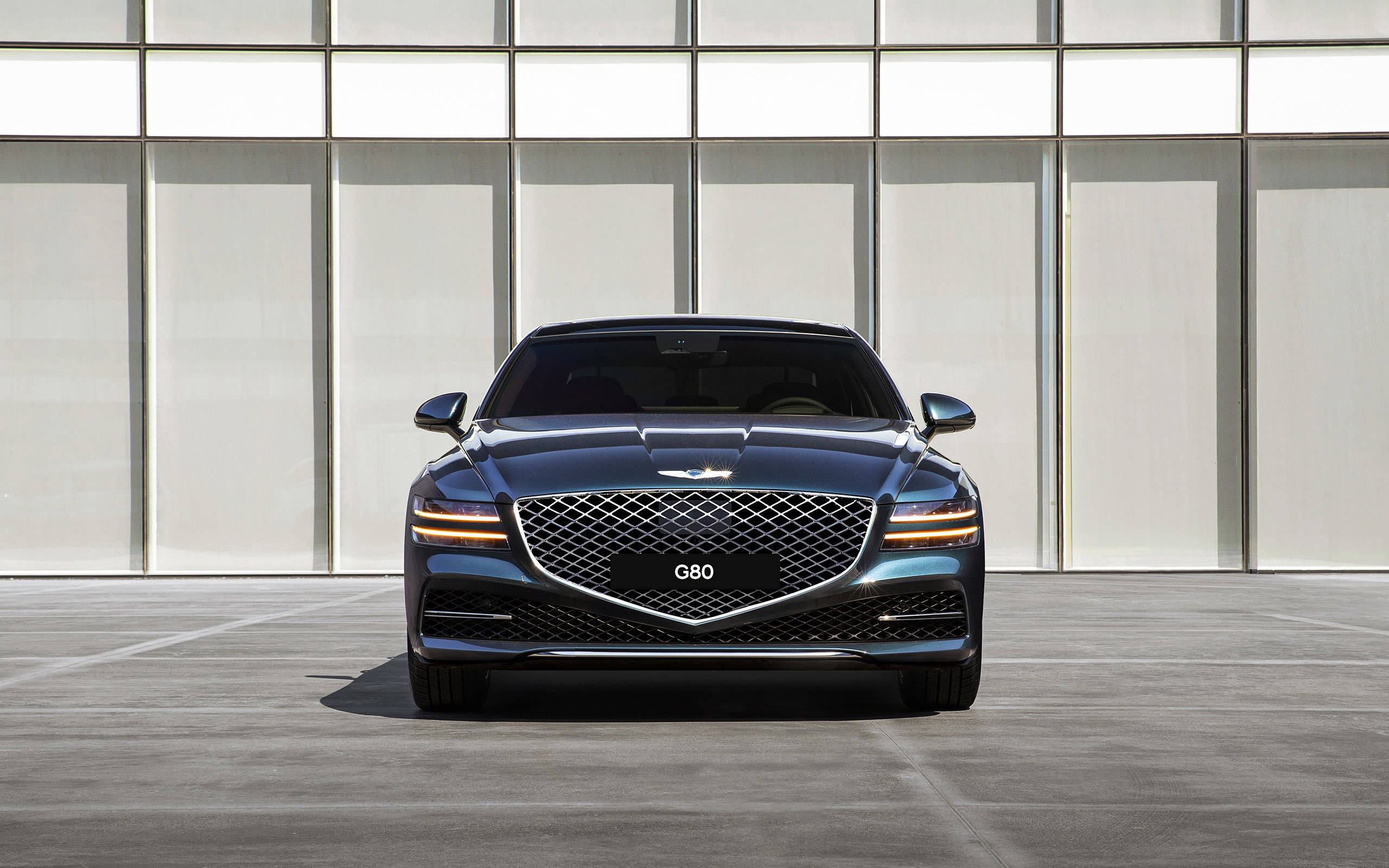 Genesis 桌布 壁紙 — 一輛時尚的深藍色 Genesis G80 豪華轎車面向現代玻璃和金屬建築外牆。