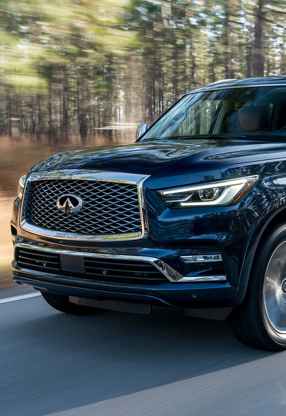 Infiniti Qx80 桌布 壁紙 — 一輛時尚的深藍色 Infiniti SUV 沿著森林道路疾馳，動態模糊傳達出動感。