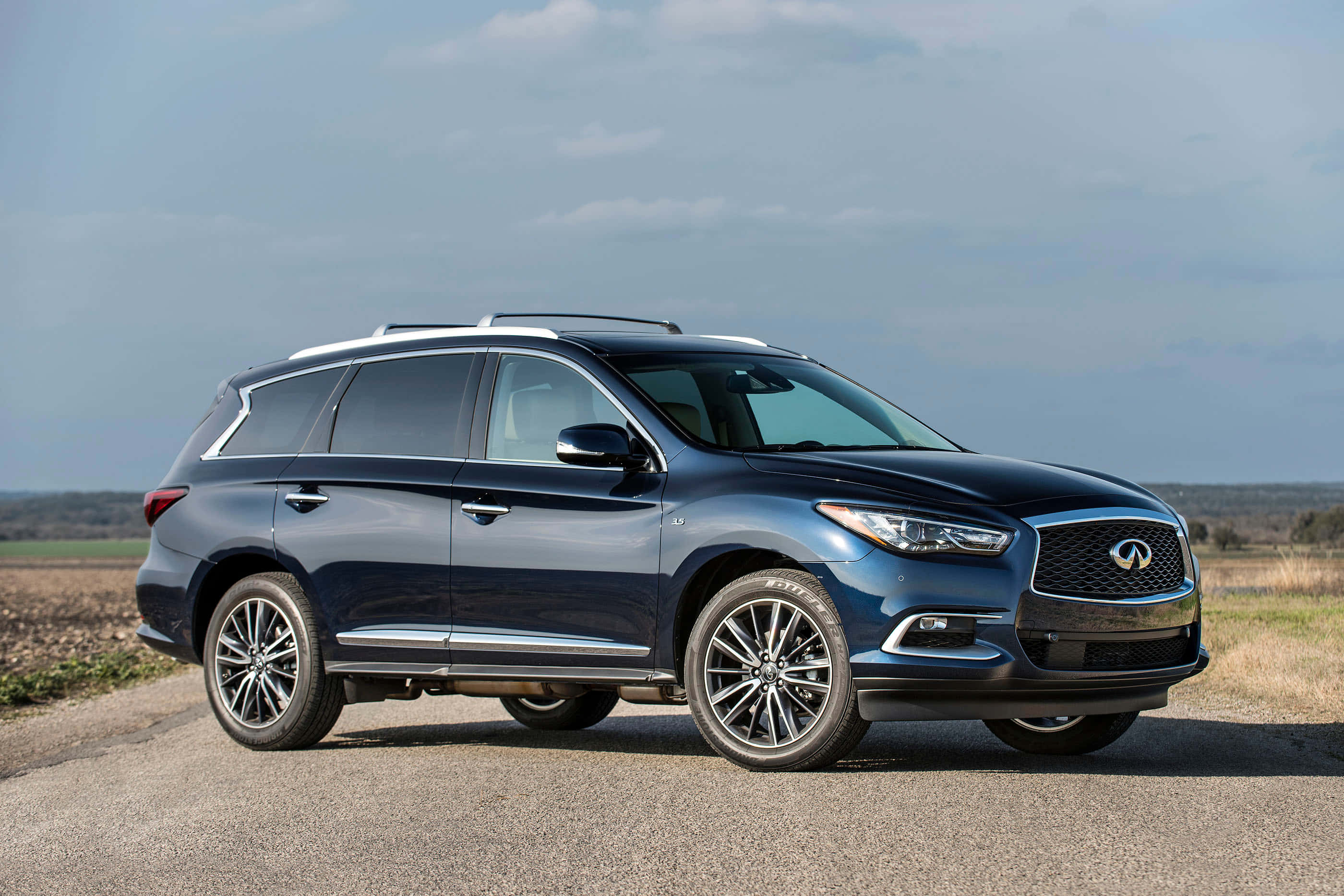Infiniti Qx60 桌布 壁紙 — 一輛時尚的深藍色 Infiniti QX60 SUV 停泊在碎石路上，天空多雲，背景是開闊的田野。