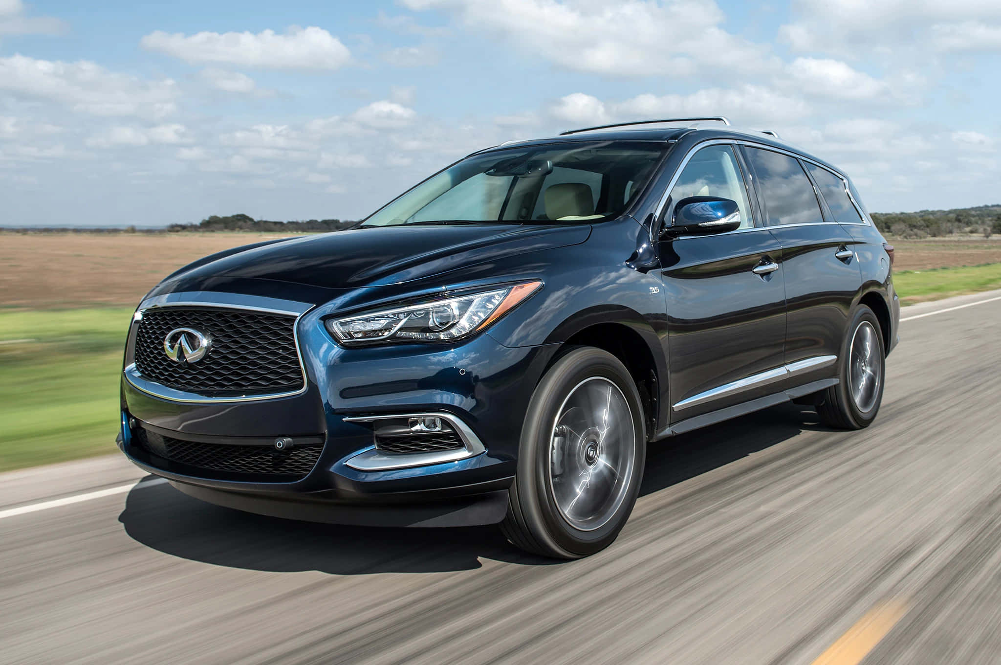 Infiniti Qx60 桌布 壁紙 — 一輛時尚的深藍色 Infiniti SUV 在陽光明媚的高速公路上疾馳，背景是模糊的綠色田野和多雲的天空。