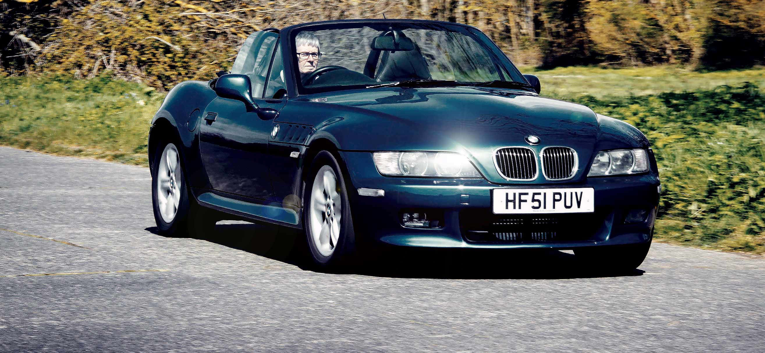 Bmw Z3 桌布 壁紙 — 一輛時尚的深藍色BMW Z8敞篷跑車沿著蜿蜒的鄉村道路行駛，背景是秋天的樹葉。